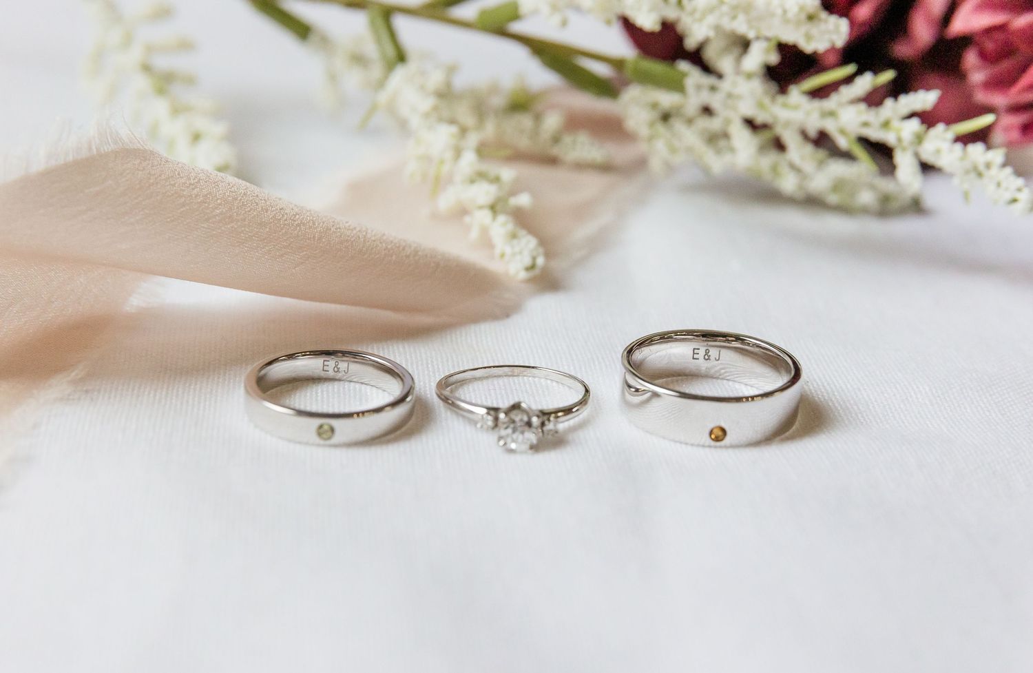 Silver wedding rings displayed in a row on white fabric with soft pink and white flowers in the background.
