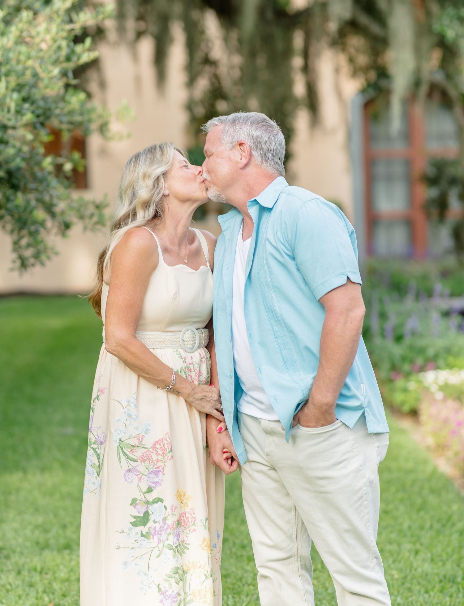 A romantic couple in white and blue outfits embrace and share a tender moment in a lush garden setting.
