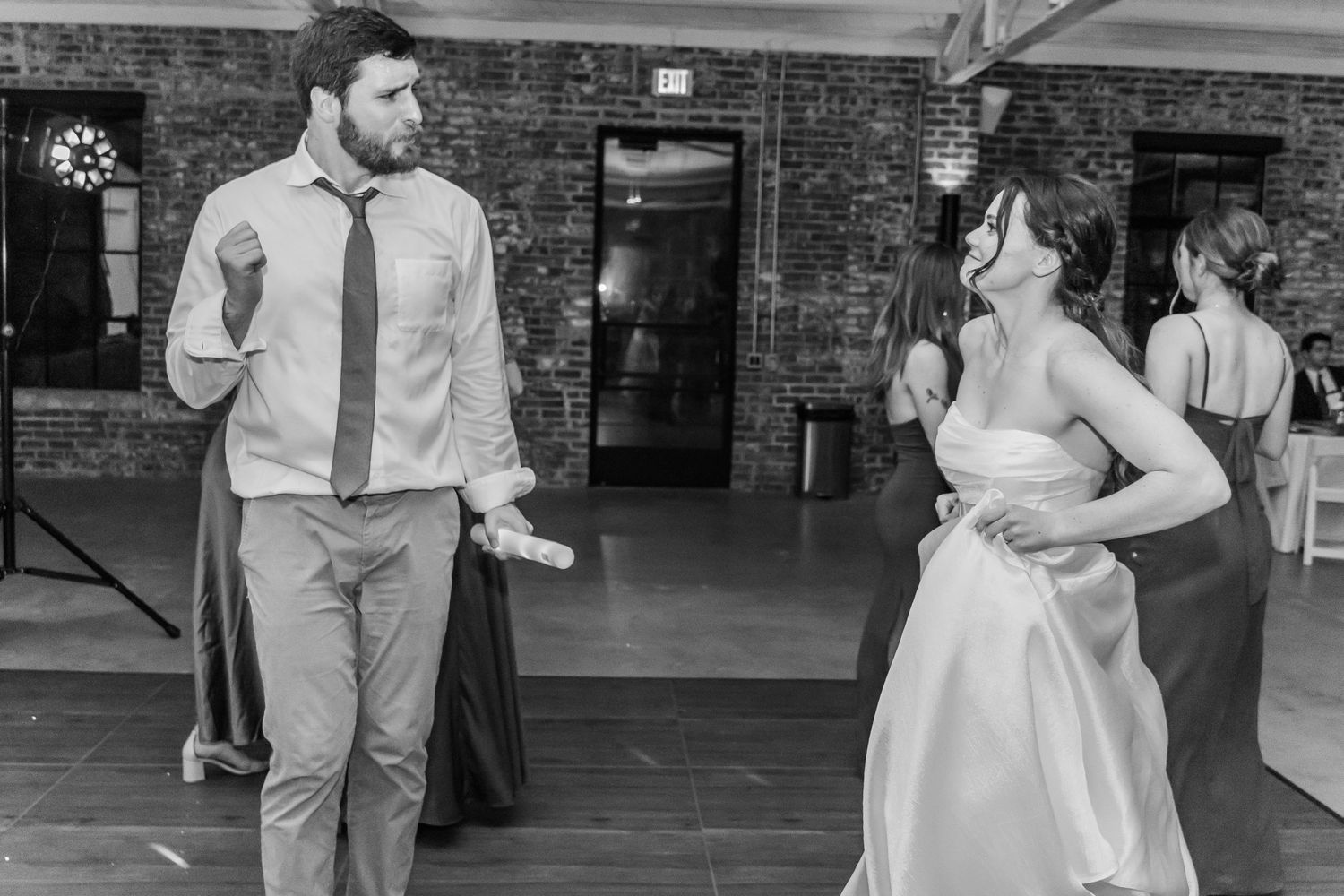A couple dances together in a rustic industrial venue with exposed brick walls during a wedding celebration.
