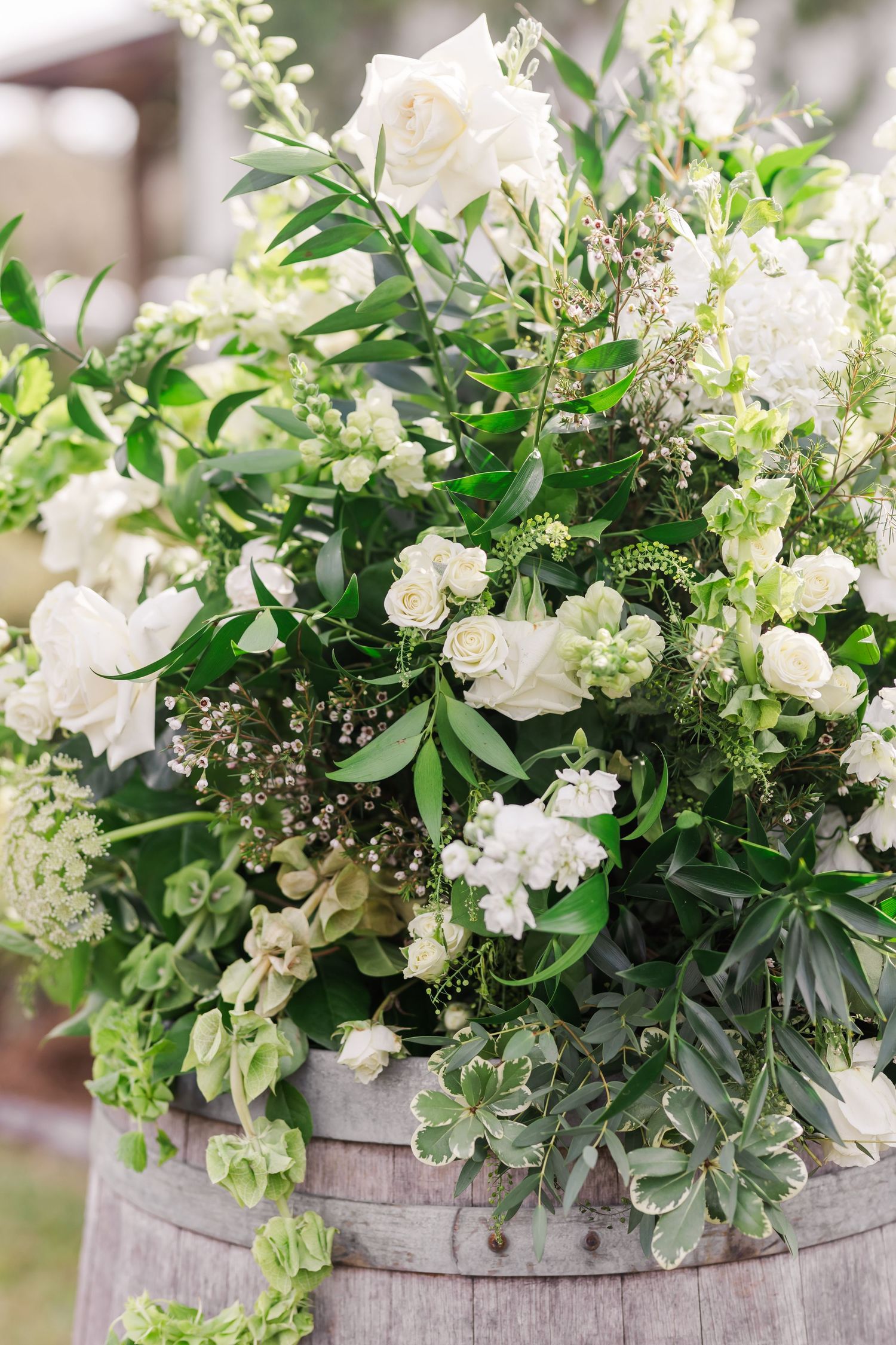 White roses and greenery arranged in a weathered wooden barrel planter for wedding decor.