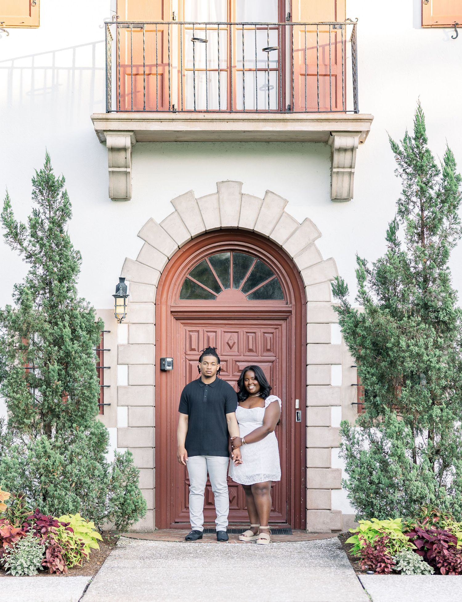Elegant engagement portrait in front of Mediterranean-style architecture.