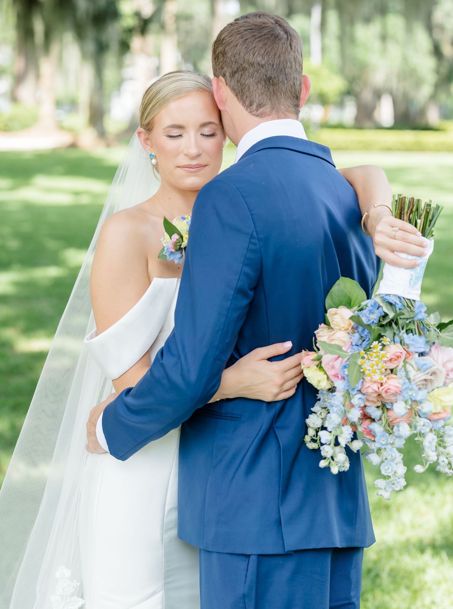 A romantic first look moment between newlyweds in a sunlit garden setting, with the bride holding a pastel bouquet.