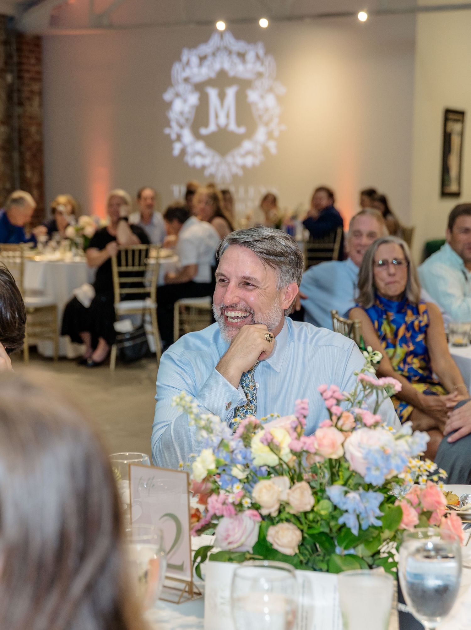 Wedding reception table decorated with pastel floral centerpieces in an elegant brick-walled venue.