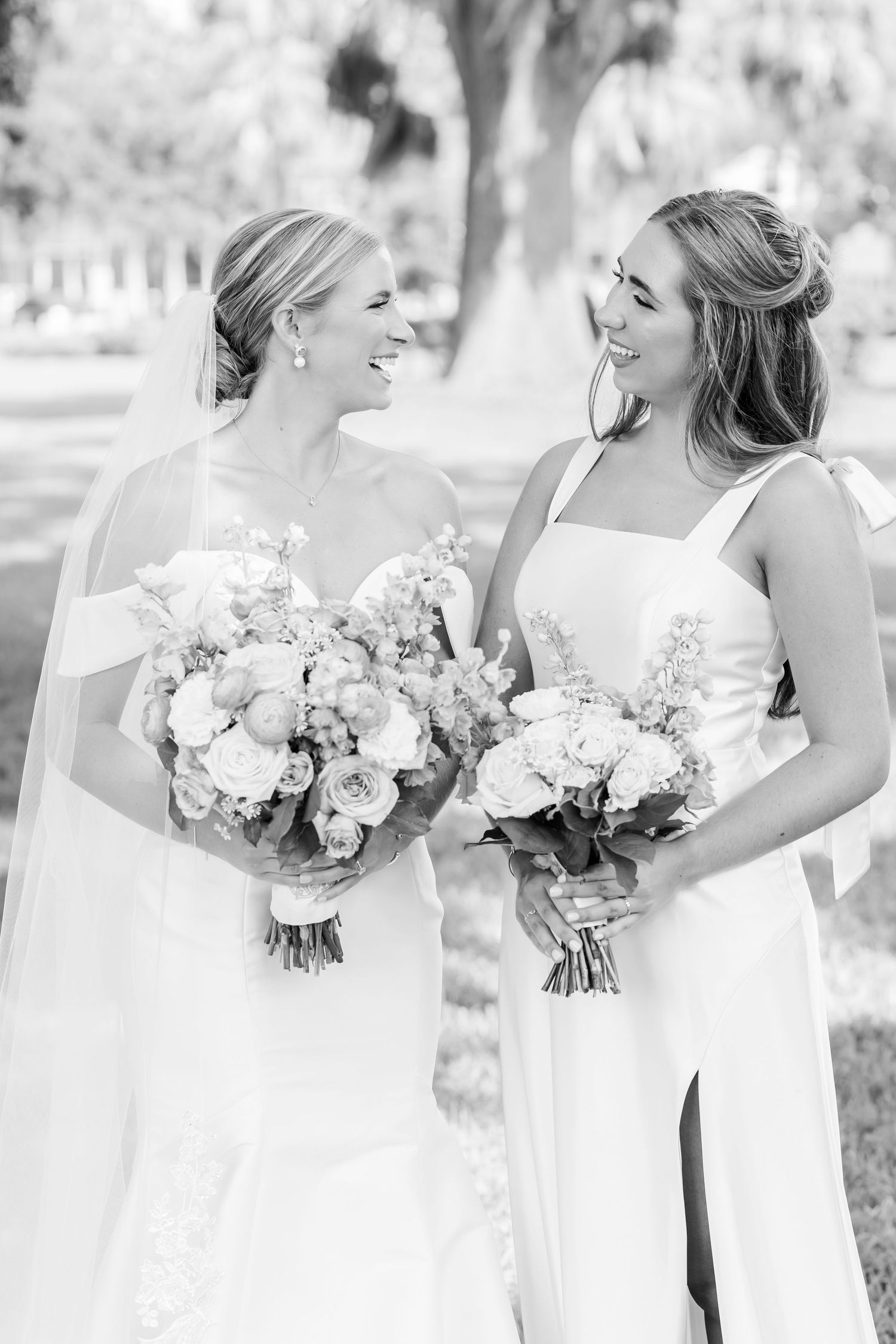 Black and white photo of bridal party holding elegant bouquets while wearing white and light colored dresses.
