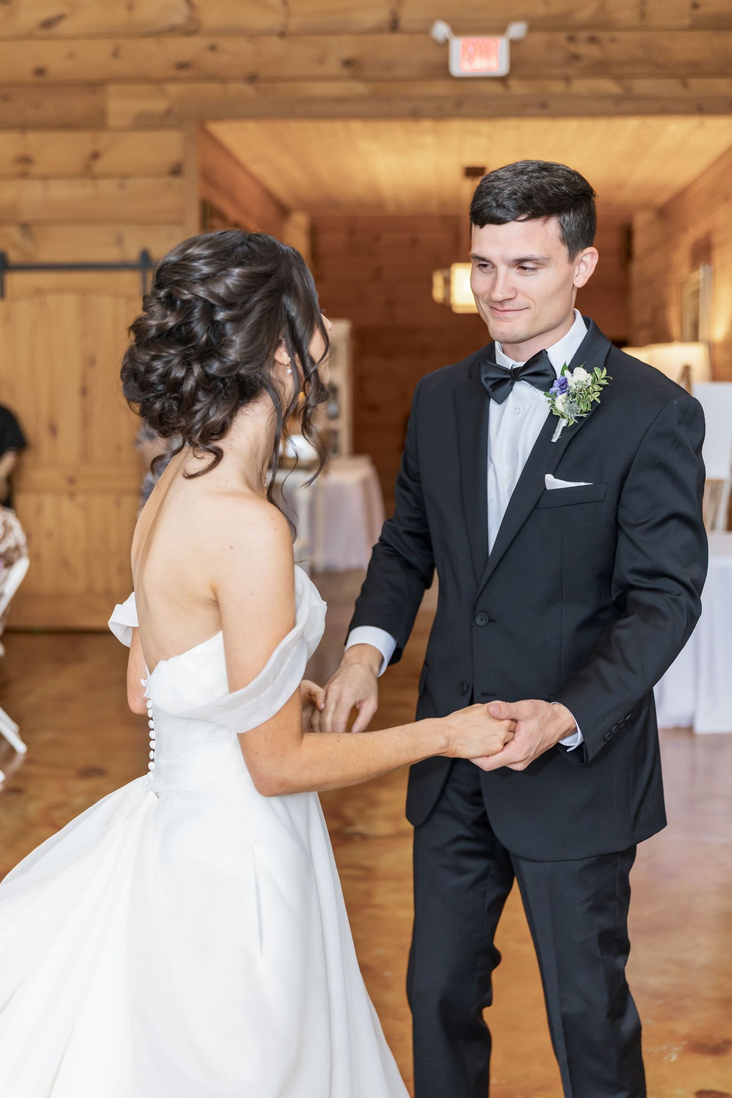 A couple shares their first dance in a rustic wooden barn venue decorated for a wedding celebration.