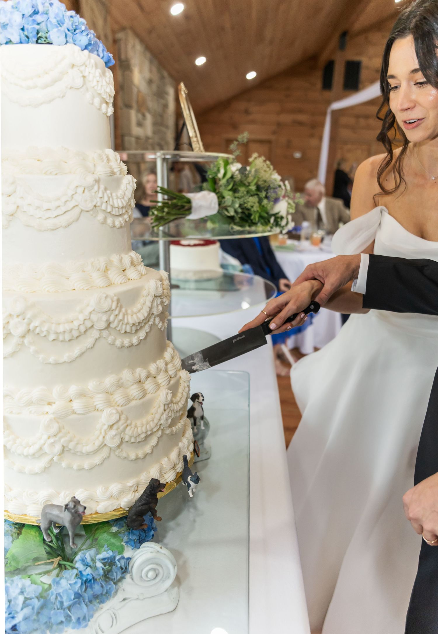 Close-up of a white tiered wedding cake with delicate lace details and blue hydrangea accents.
