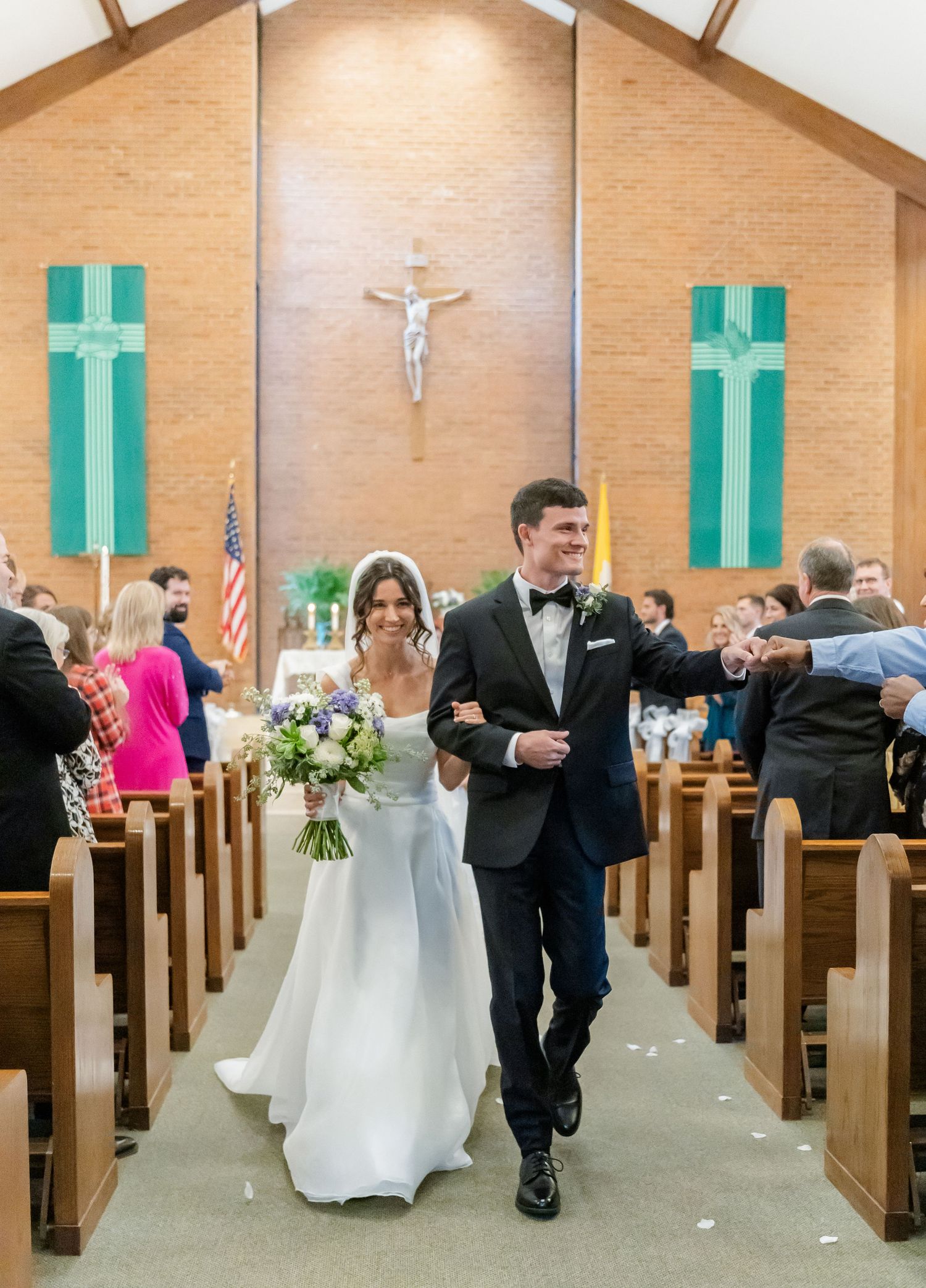 Wedding party members walking down the aisle after ceremony in brick church with green shutters.