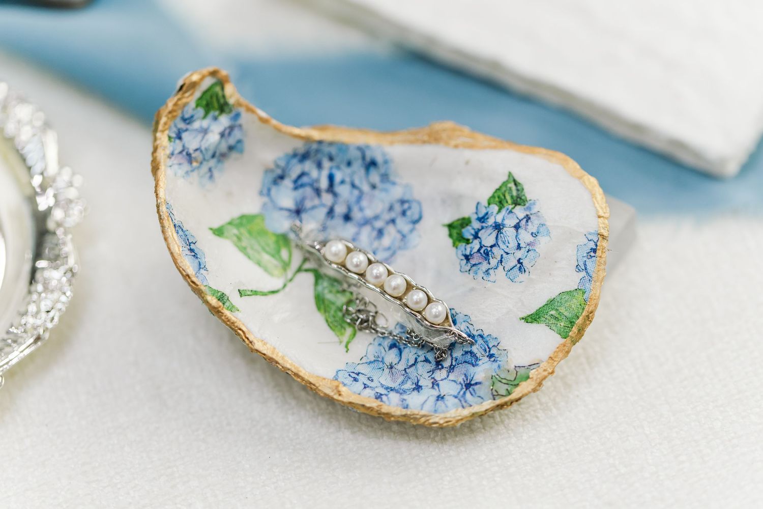 Delicate oyster shells painted with blue hydrangea flowers and gold trim arranged in an elegant display.