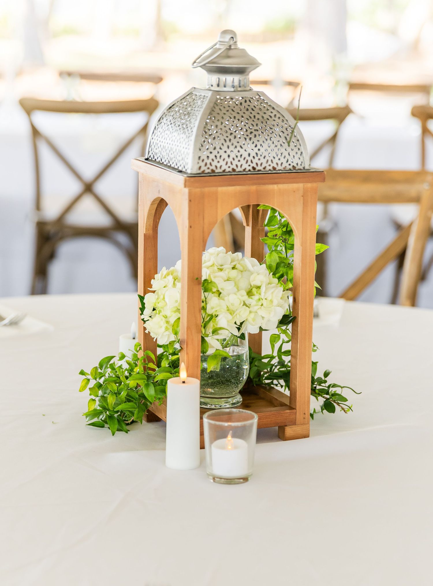 Elegant wooden lantern centerpiece with white hydrangeas and greenery on a white tablecloth.