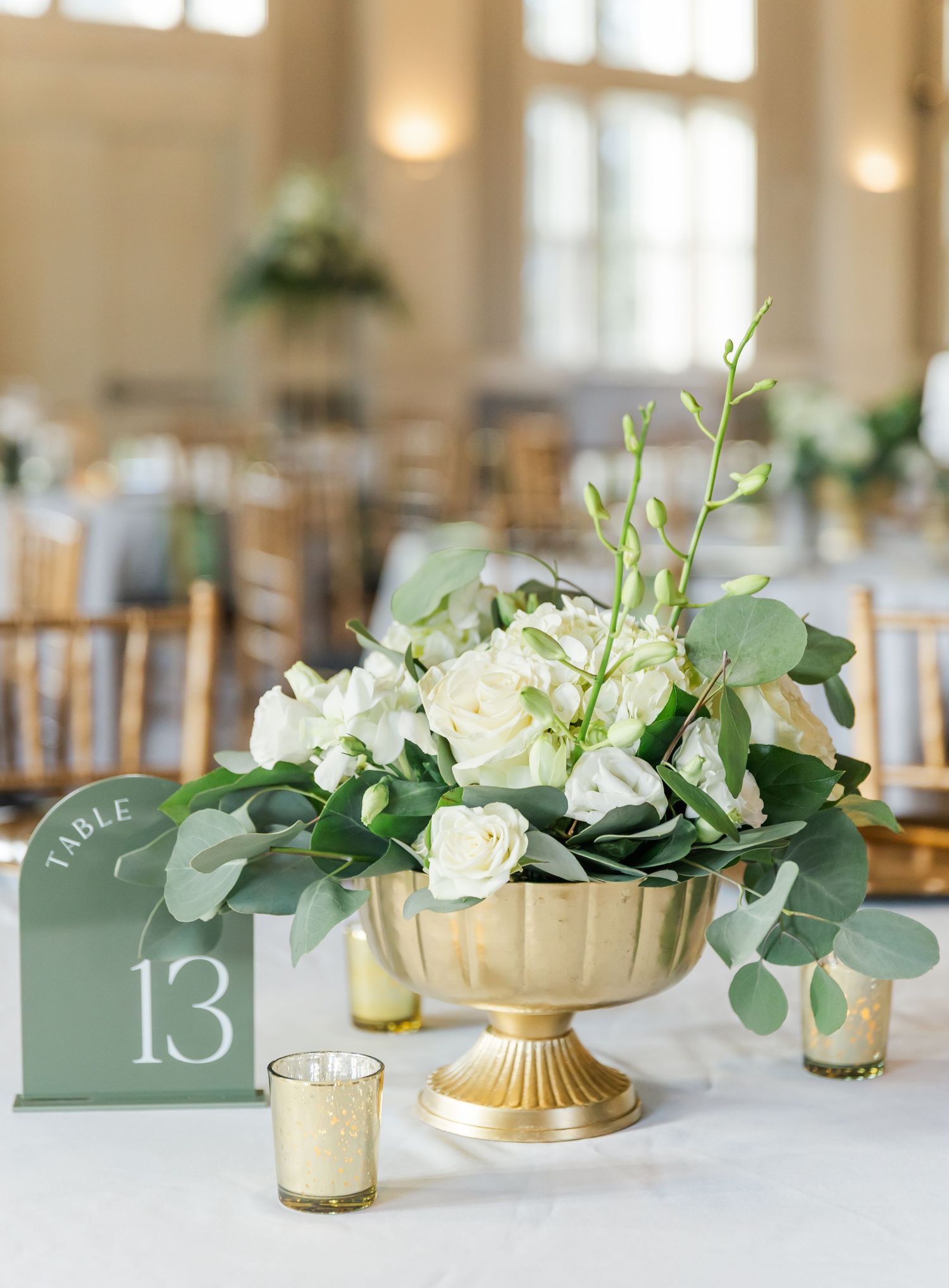 Wedding reception table settings with gold accents and white floral centerpieces featuring table number 13.
