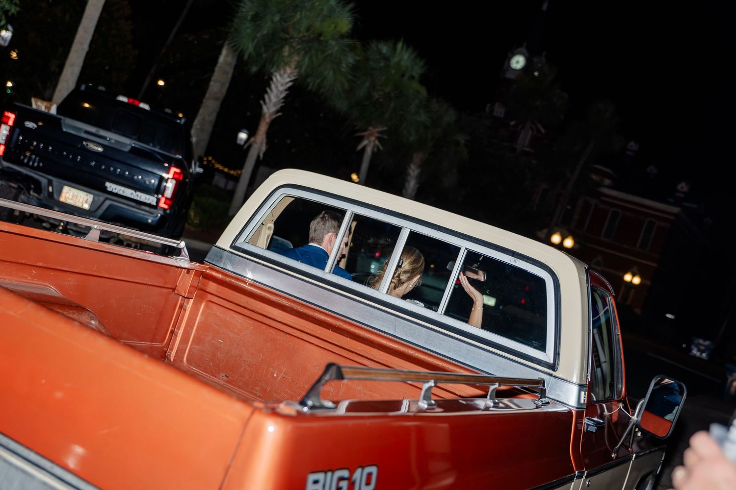 Orange and white classic car displayed at a nighttime auto show with spectators viewing the vehicle.