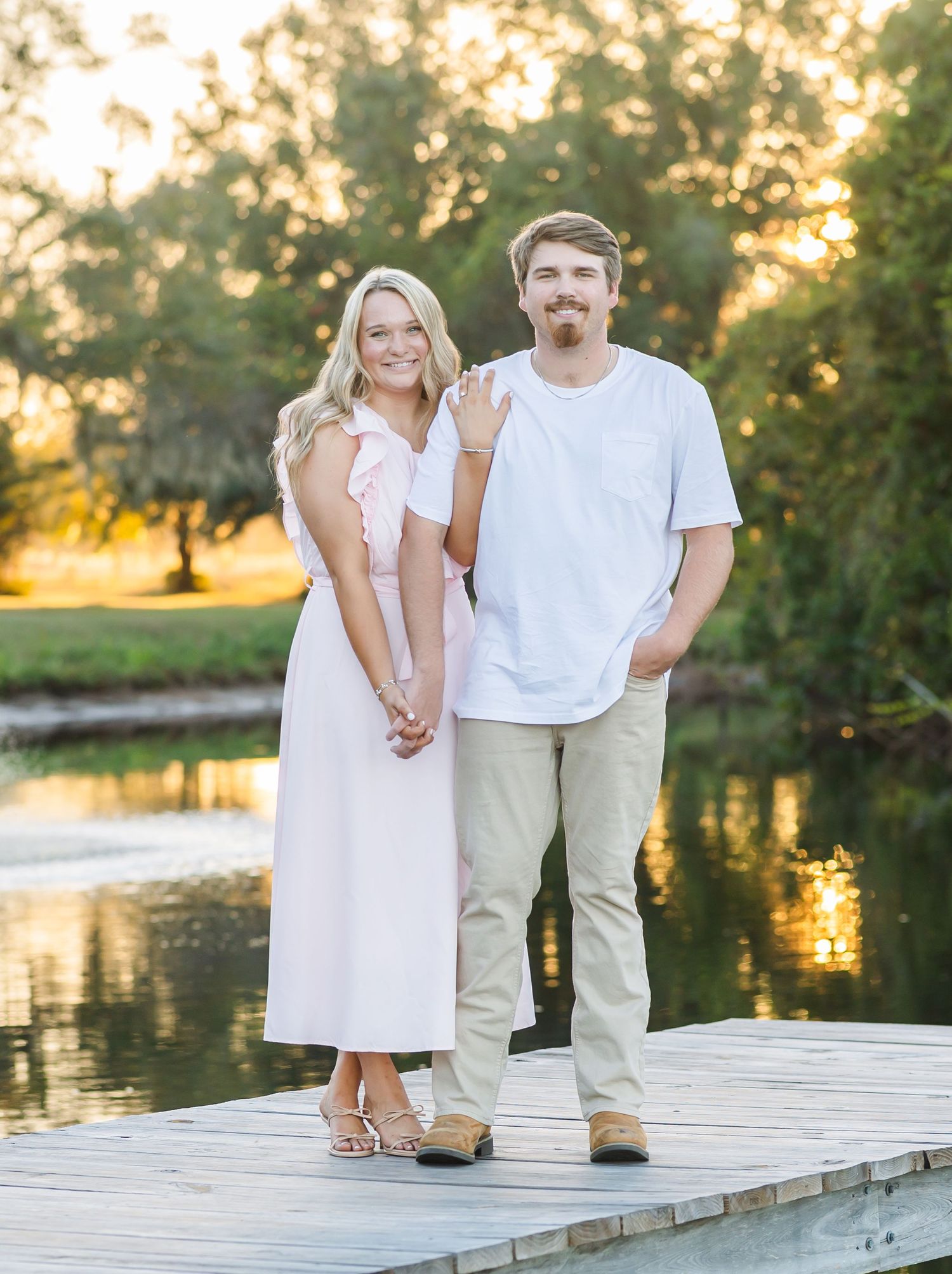 Couple sharing romantic moments on a lakeside dock during golden hour in coordinated casual outfits.