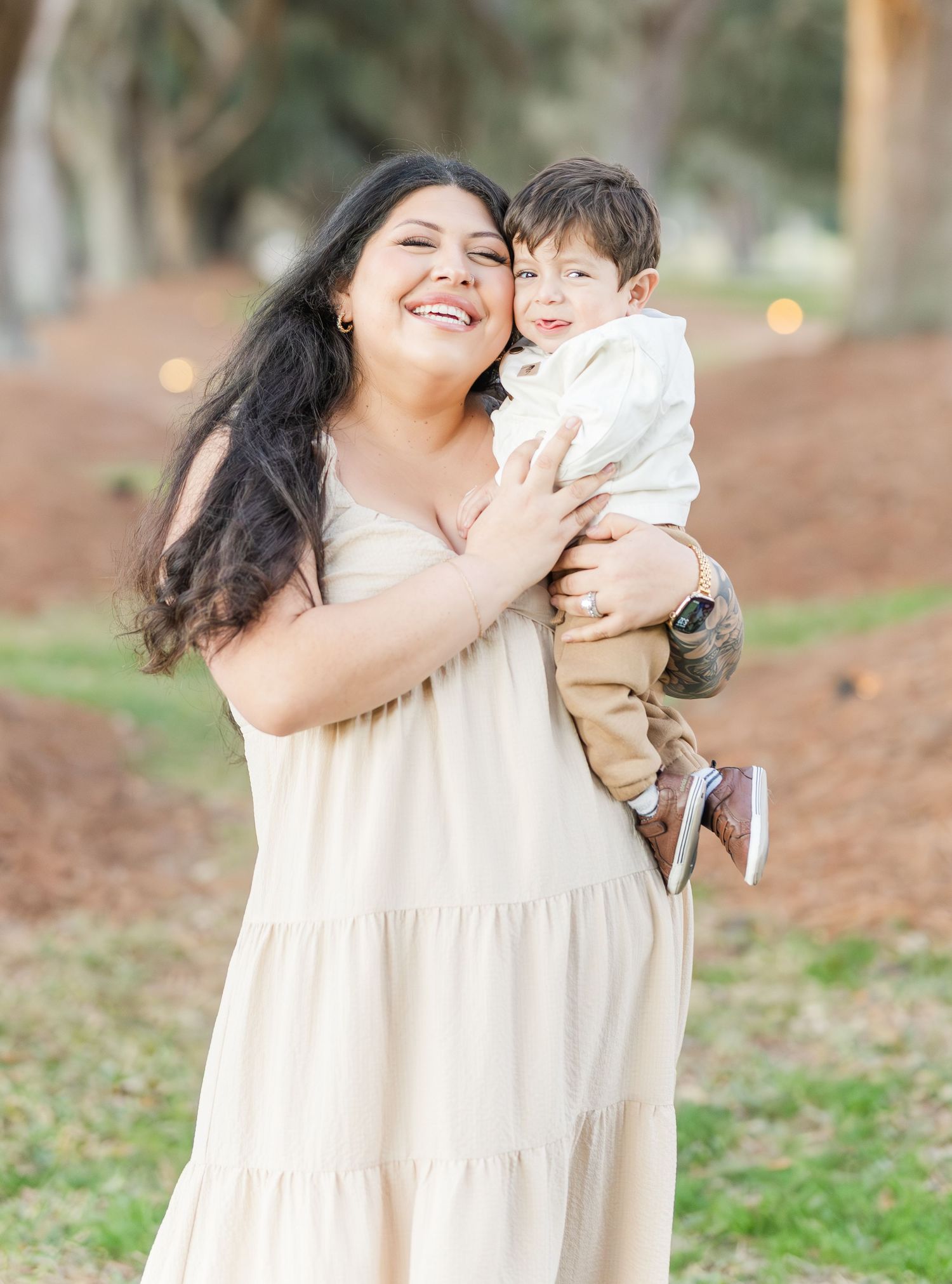 Joyful family photo session featuring cream-colored dress and natural outdoor backdrop.