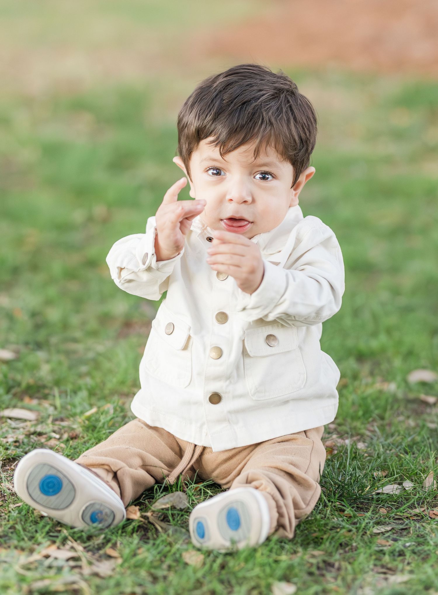 Baby in white button-up shirt and khaki pants sitting on grass during outdoor photoshoot.