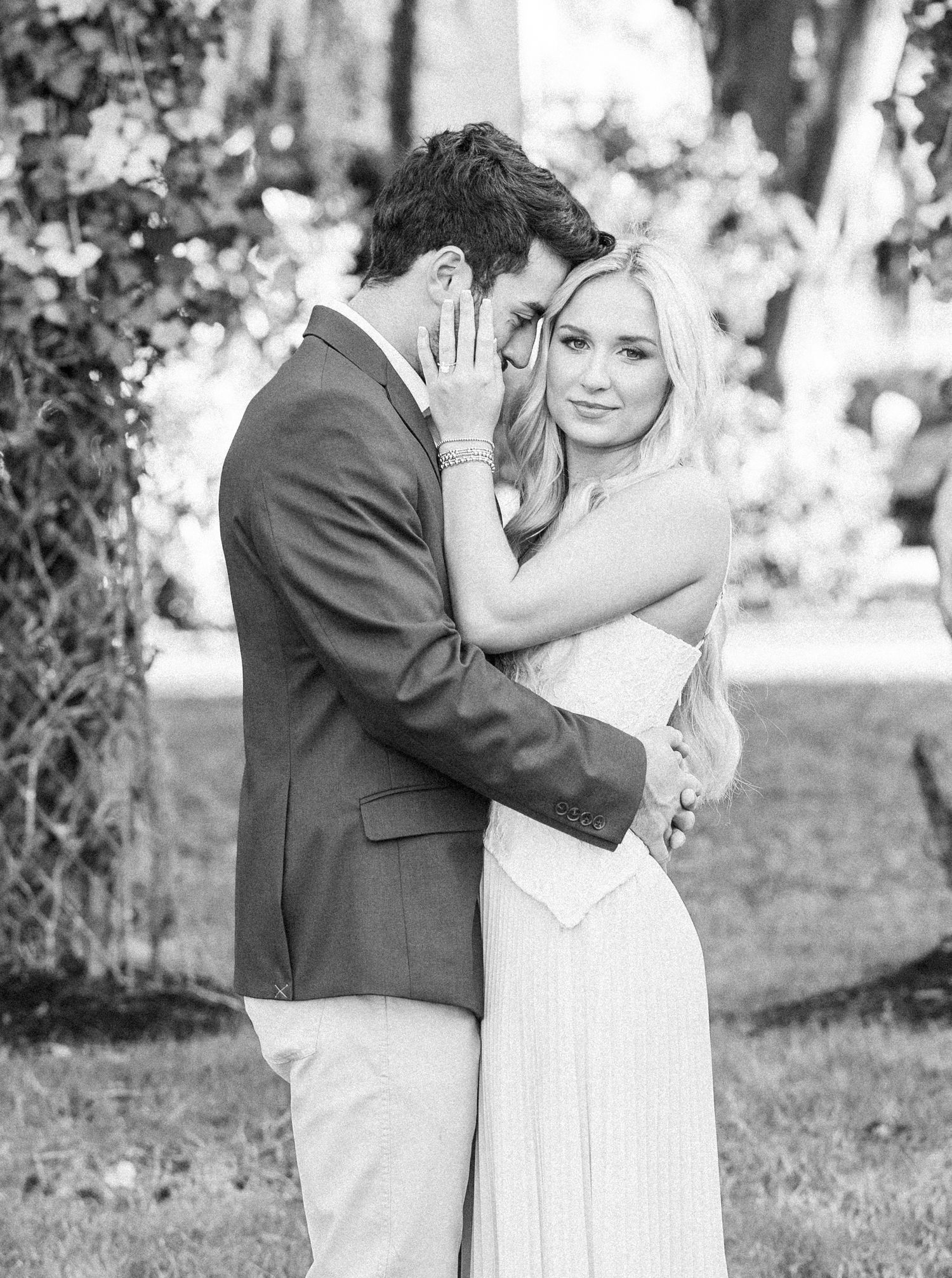 A couple shares a playful moment in black and white as they embrace outdoors in wedding attire.