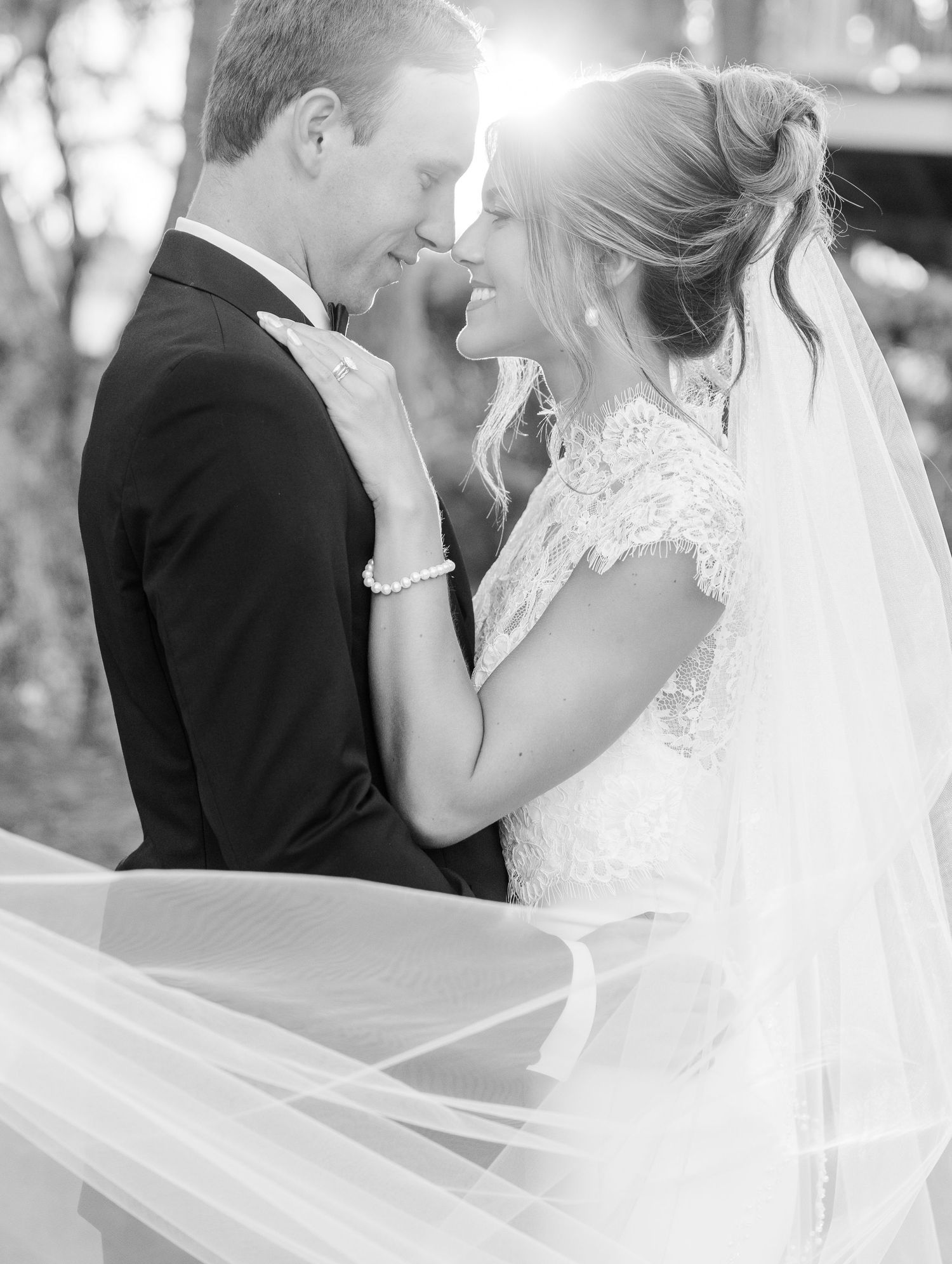 Black and white wedding photo of bride and groom sharing a romantic moment, veil flowing, lace dress, bow tie.