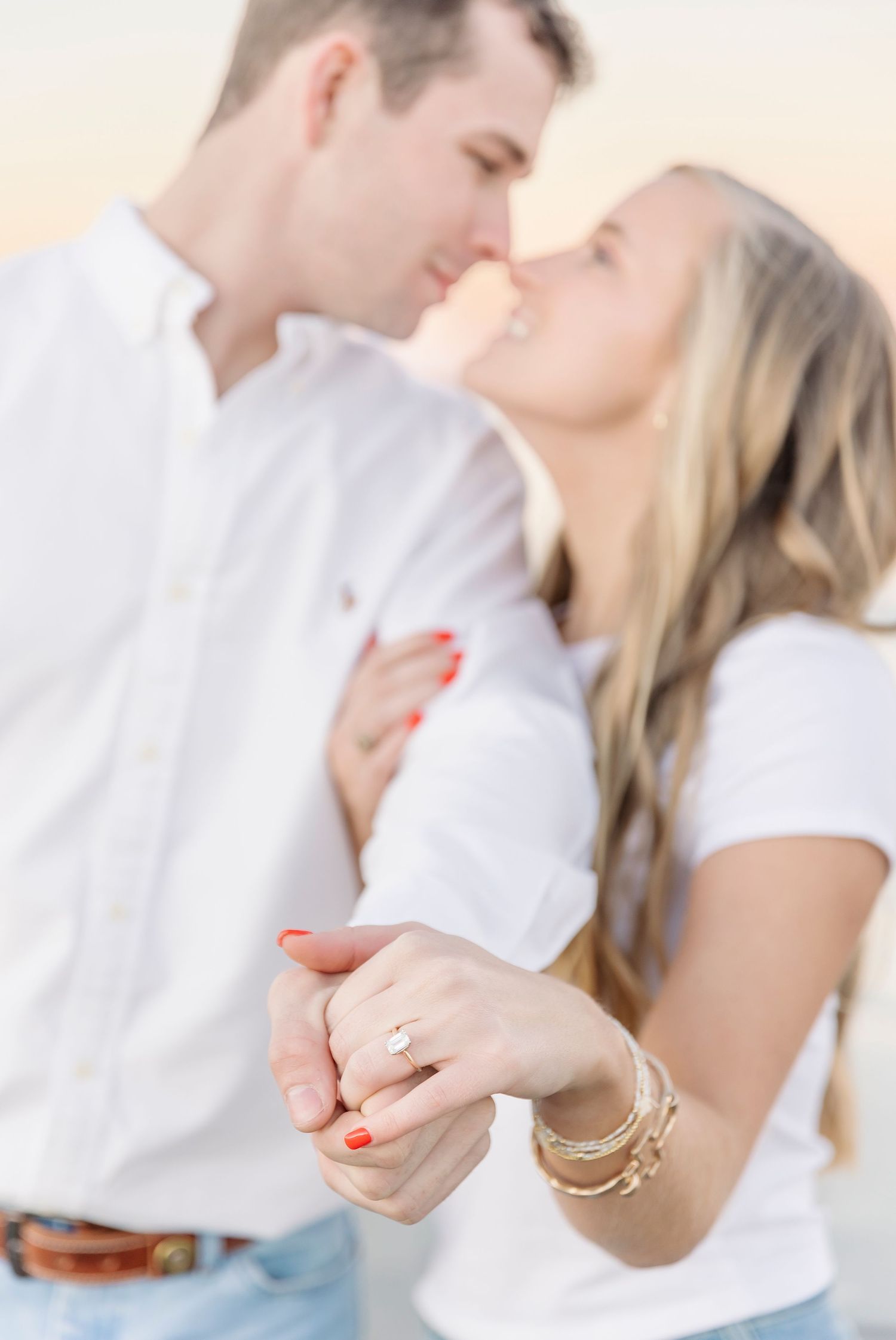 A romantic engagement photo with couple kissing while showcasing diamond ring.