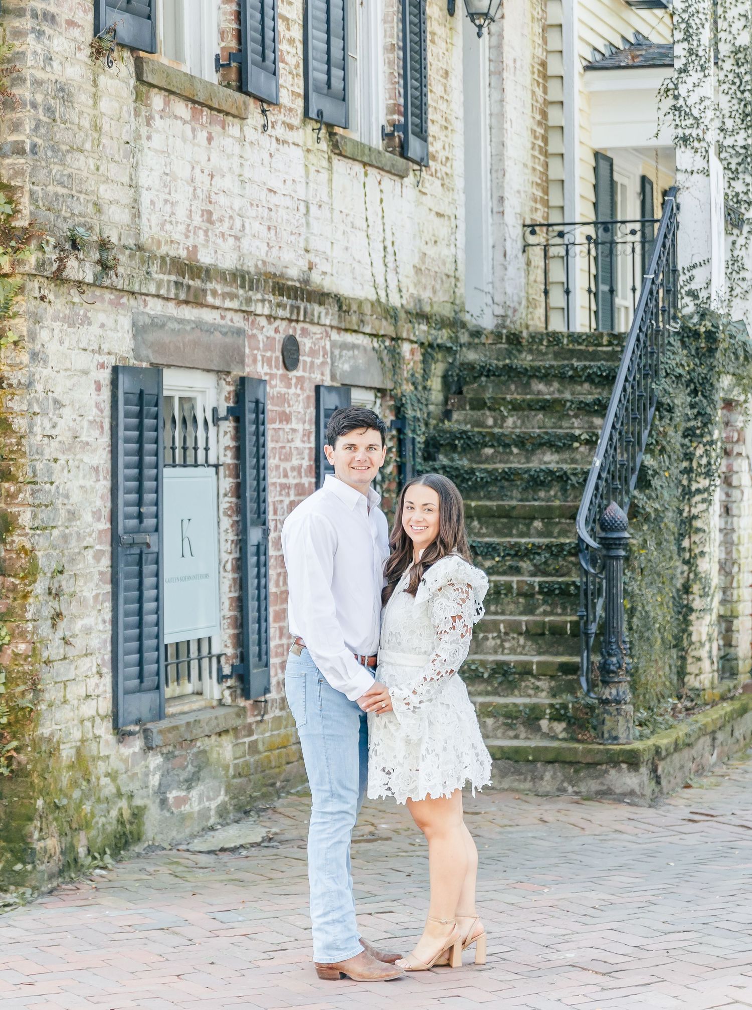 A couple poses together on brick pavement in front of historic stone steps.