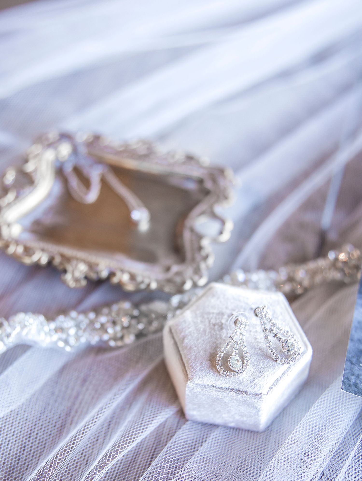 Elegant white hexagonal ring box and ornate mirror on delicate tulle fabric.