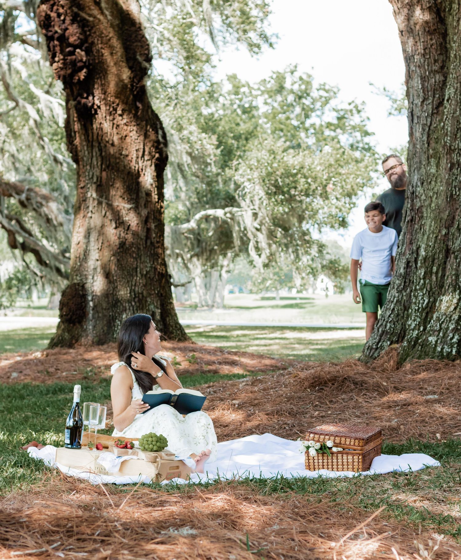 Family enjoying a picnic setup beneath large oak trees with Spanish moss.