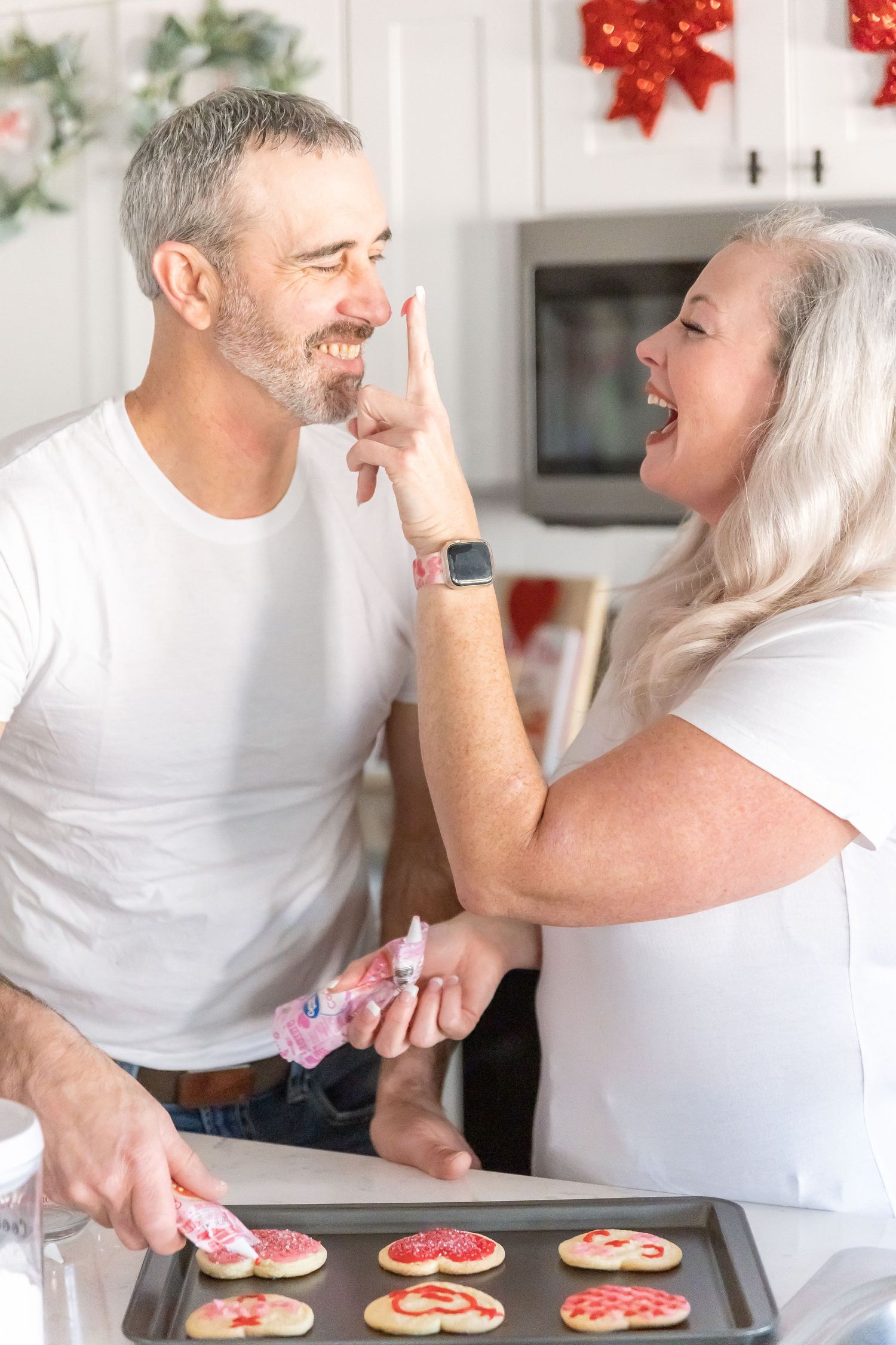 Playful couple having fun while baking Christmas cookies in decorated kitchen.