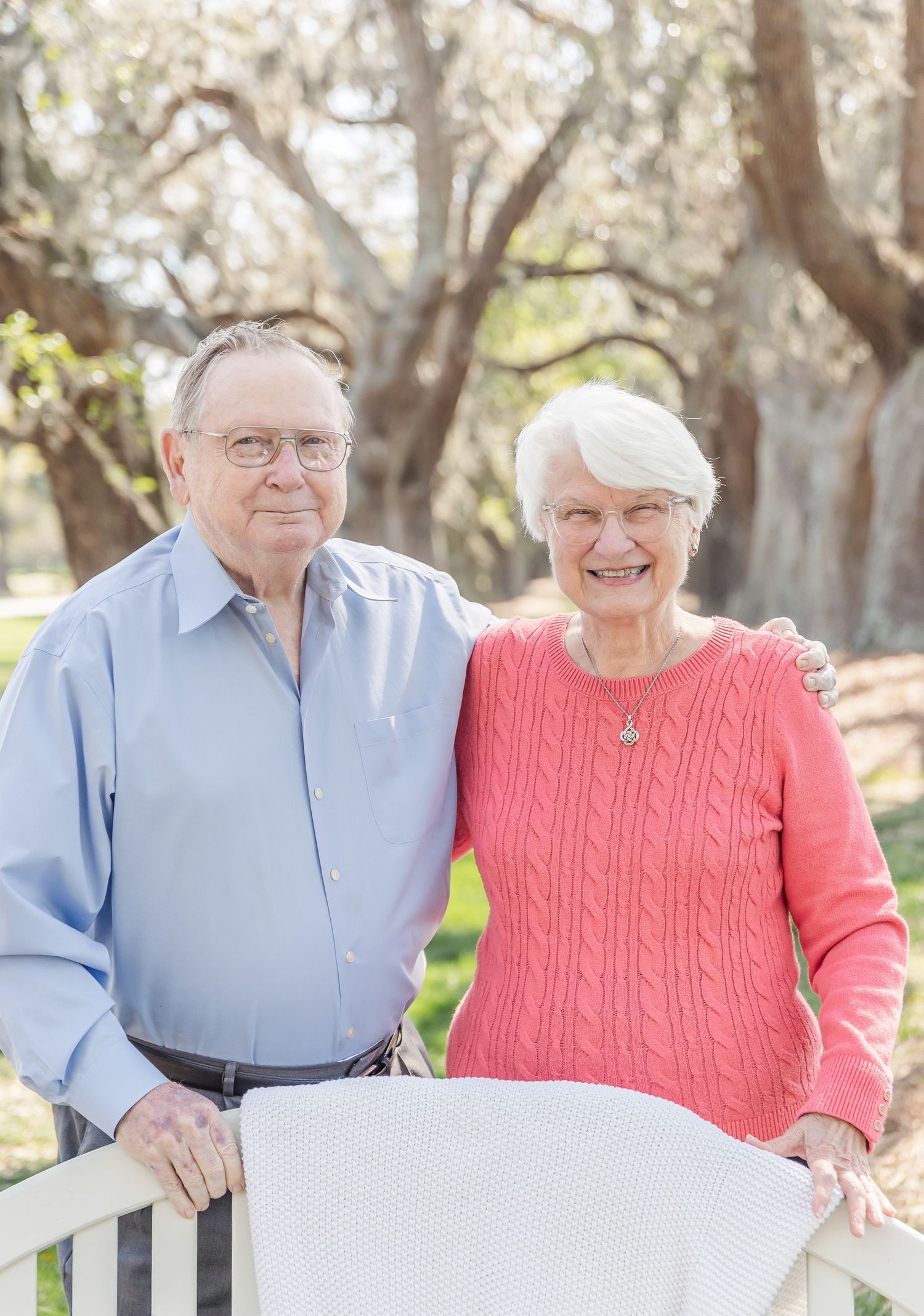 Senior couple in blue and coral sweaters pose together at outdoor park.