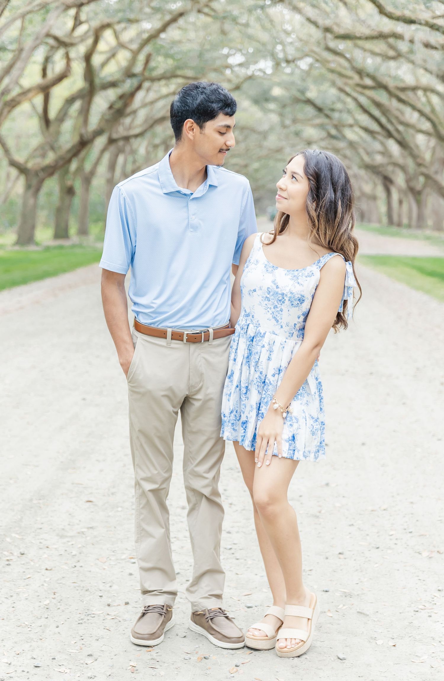 Couple in matching blue outfits share intimate moment on tree-canopied dirt road.