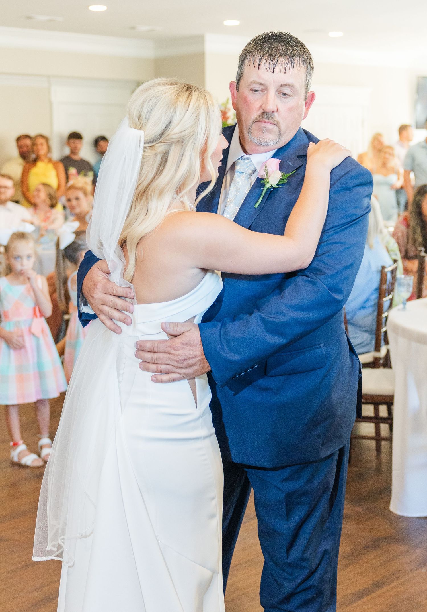 Bride shares a tender father-daughter dance at wedding reception in bright indoor venue.