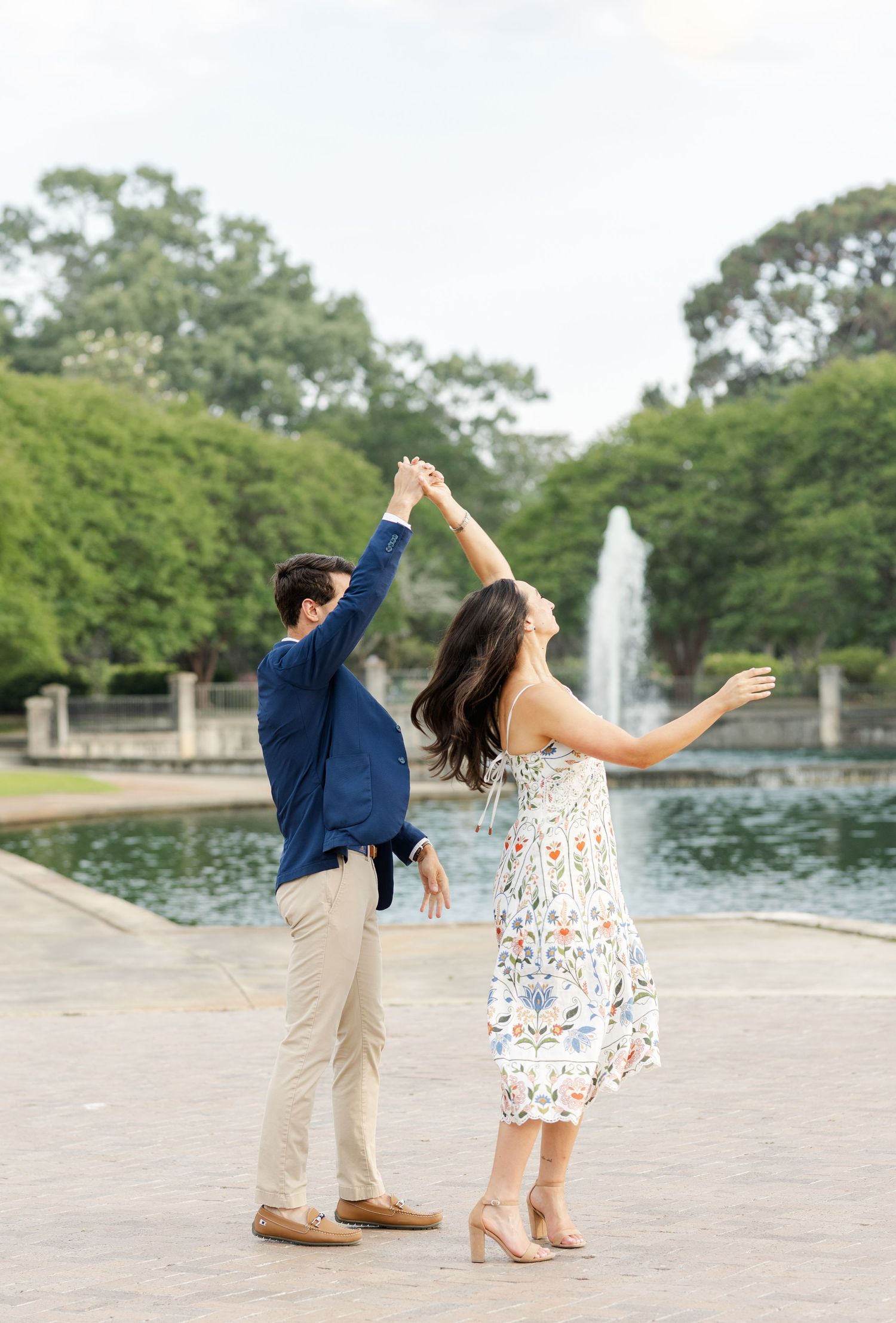 Couple dancing and spinning by a fountain outdoors during a romantic engagement photo session.