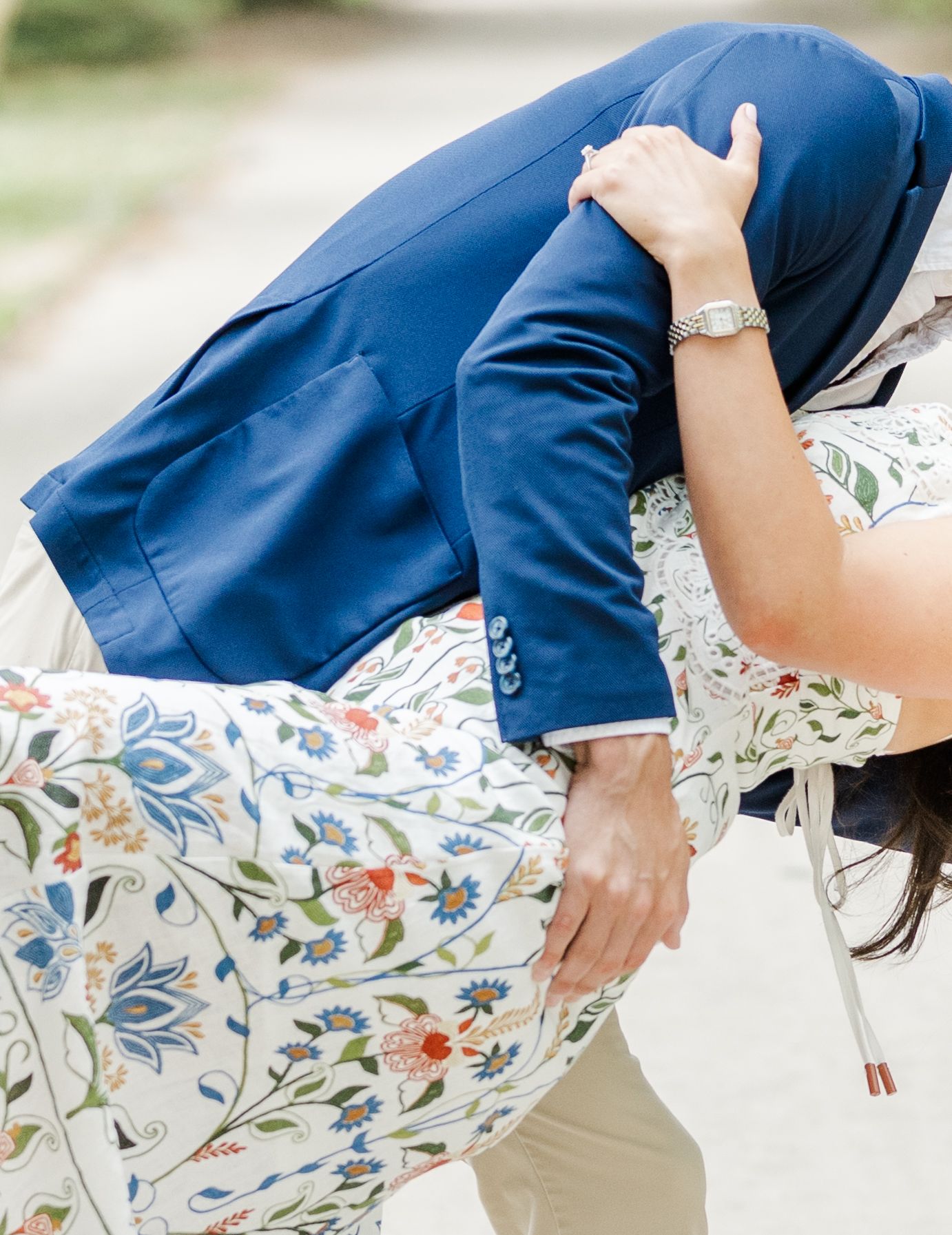 Couple embracing in a dip pose, wearing a blue suit and floral dress, captured in a romantic outdoor setting.