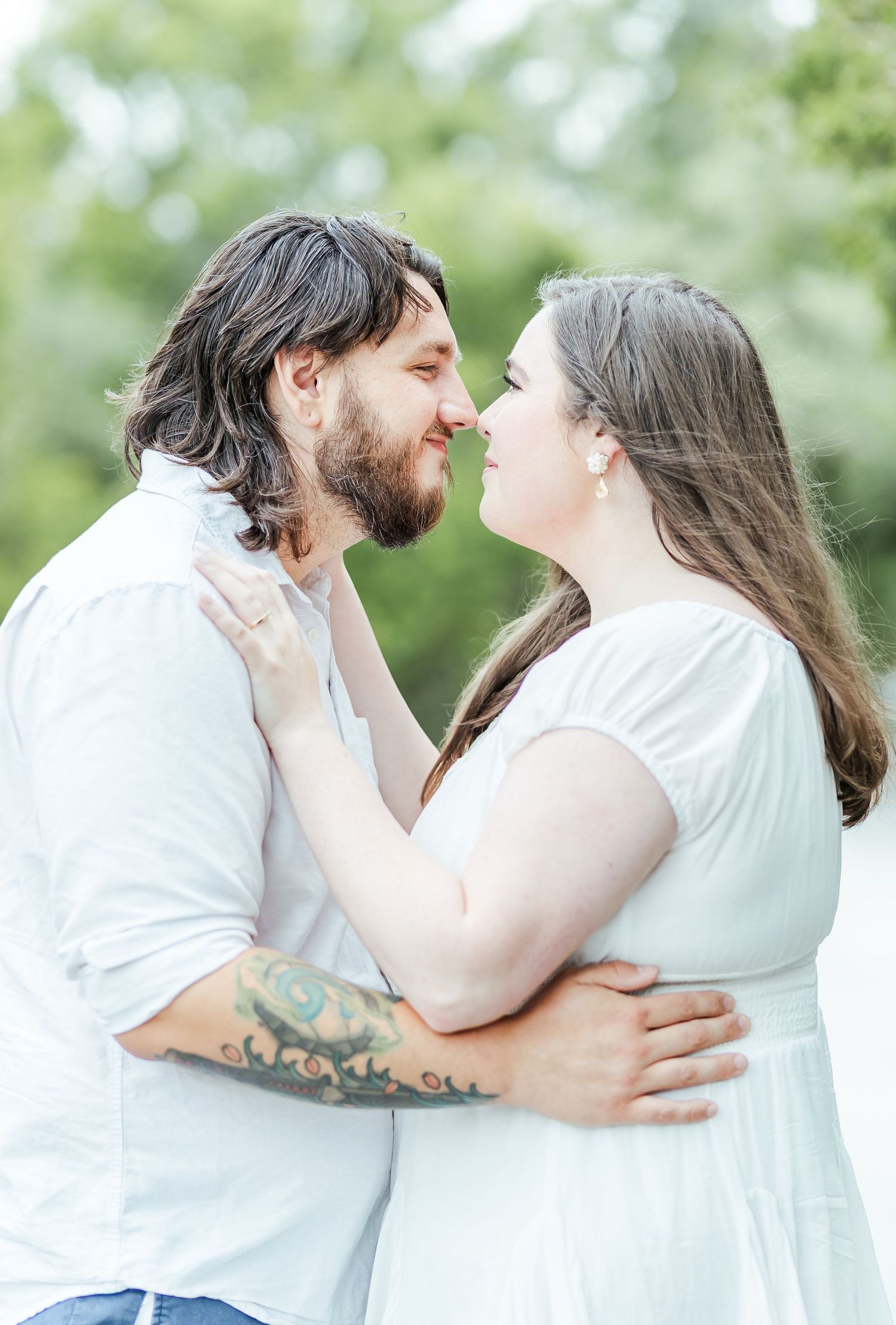Couple shares a loving moment in white outfits against a natural green background.
