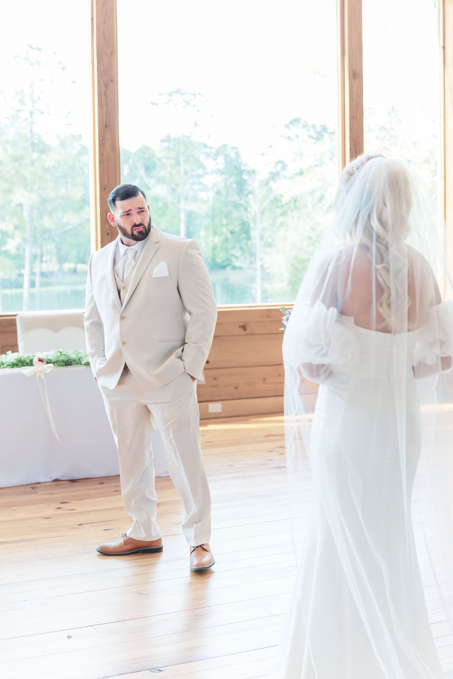 A first look wedding moment captured in a bright venue with large windows and wooden walls.