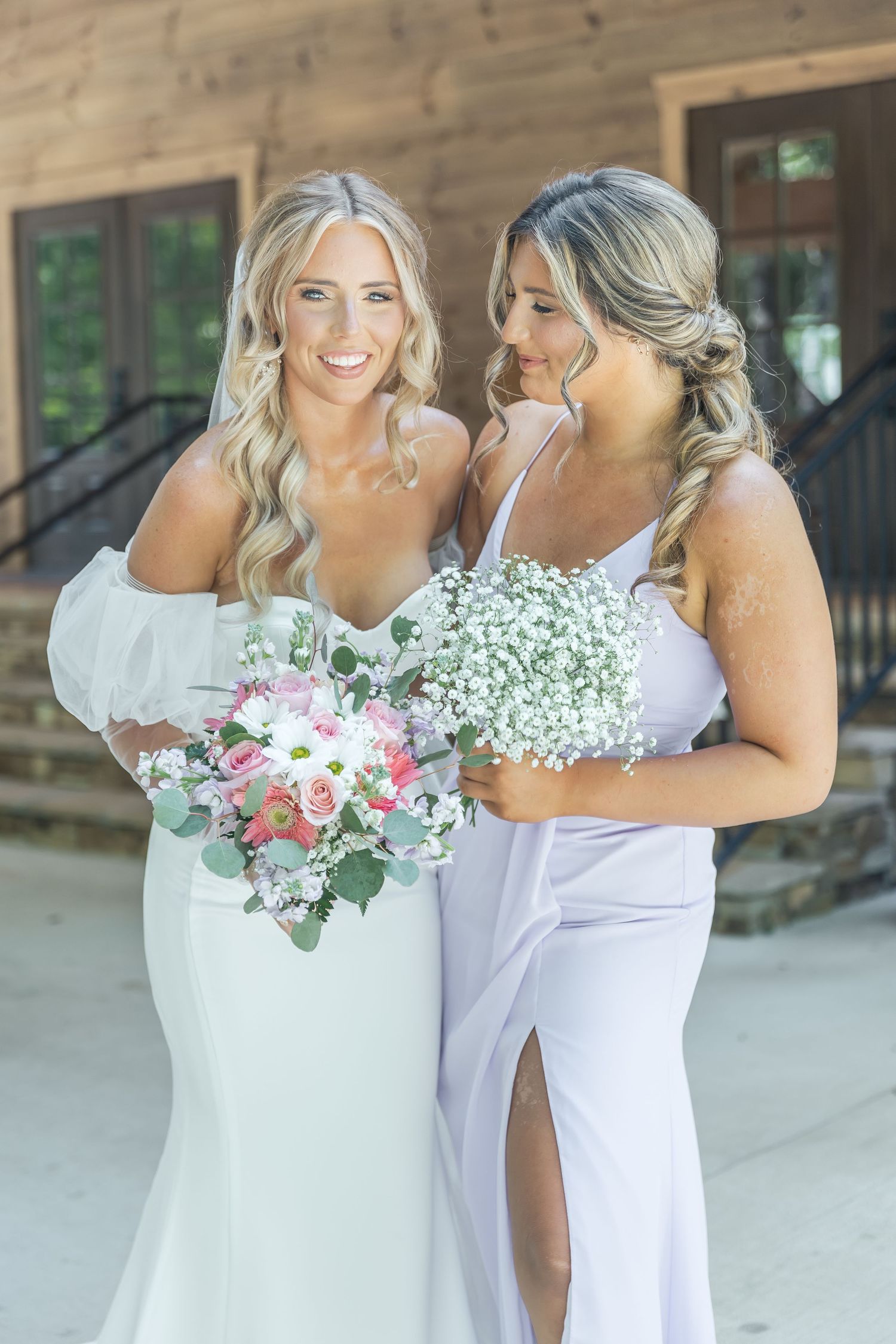 Wedding party members smile while holding bouquets against rustic wood backdrop.