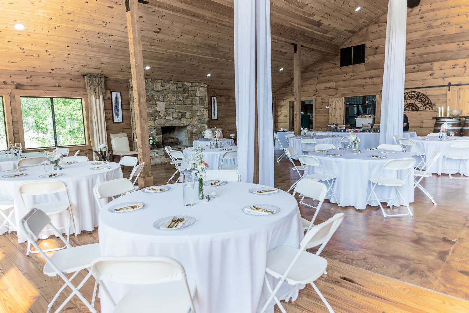 Rustic wedding reception venue with white round tables and chairs set up in a wooden barn-style interior.