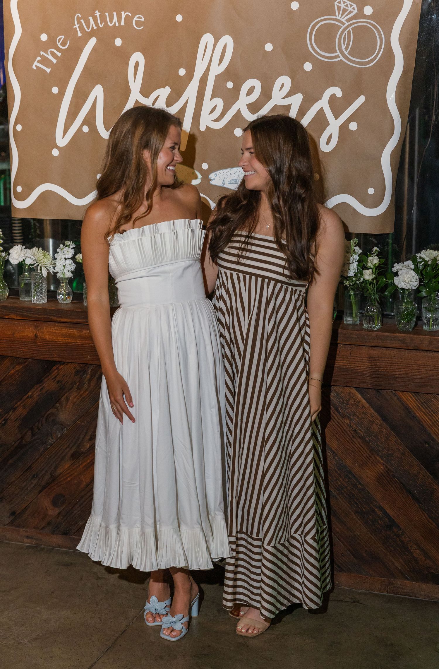Two women smiling at each other at a bridal shower in front of a 'The Future Walkers' sign.
