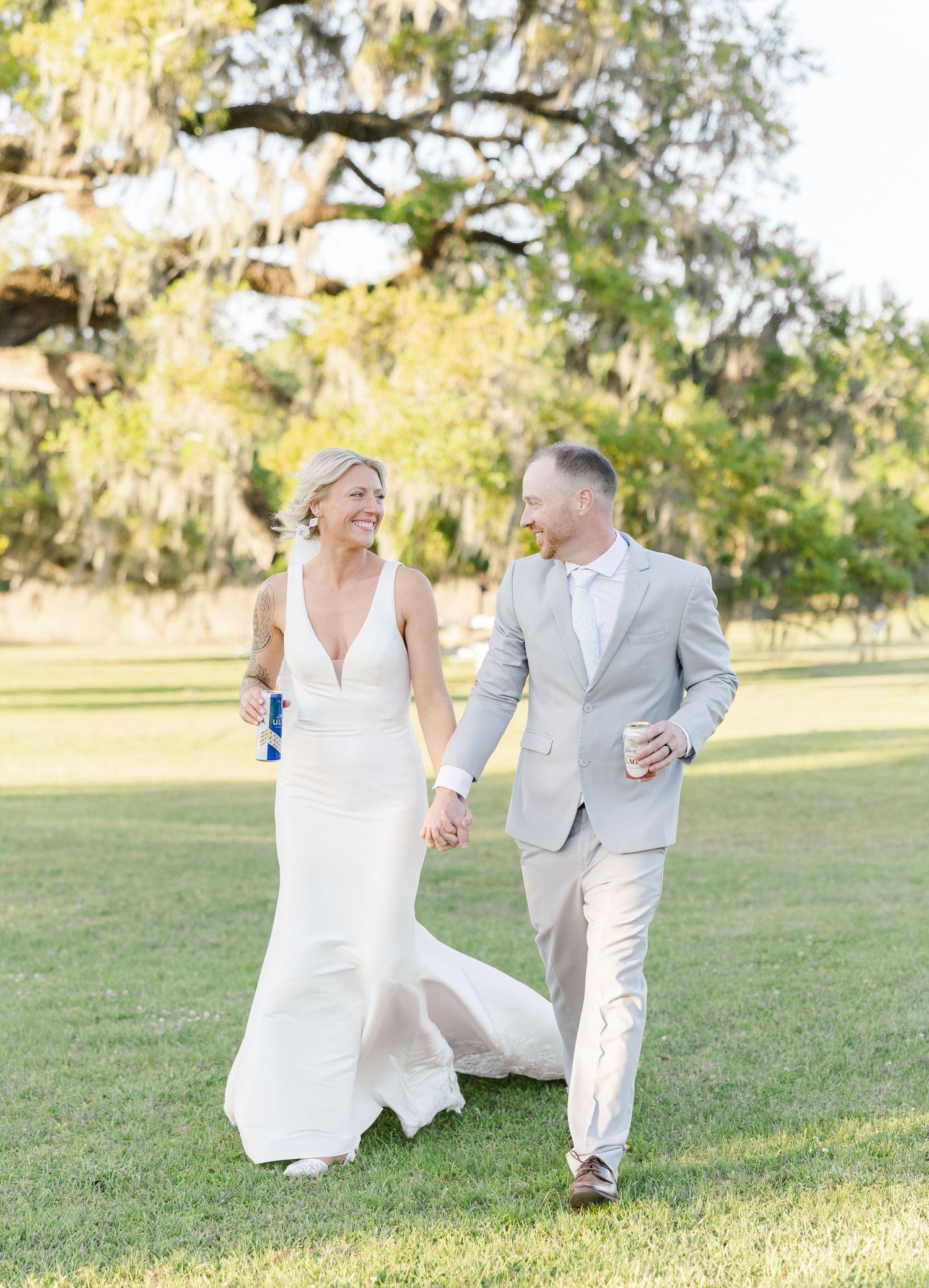Happy bride in white gown and groom in gray suit laughing while walking outdoors.
