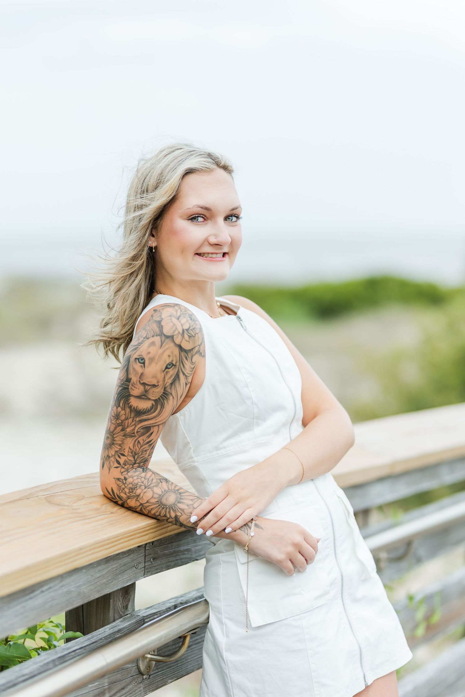 White sundress against wooden boardwalk railing with coastal vegetation in the background.