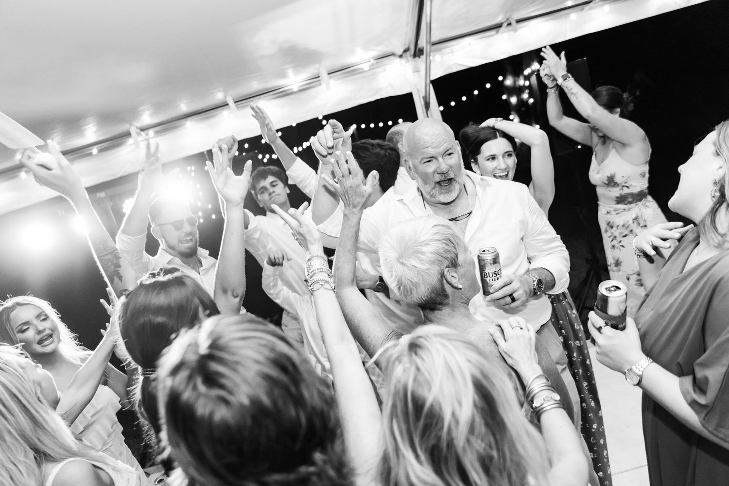 A black and white photo shows a lively dance floor with people dancing and celebrating at a wedding reception.