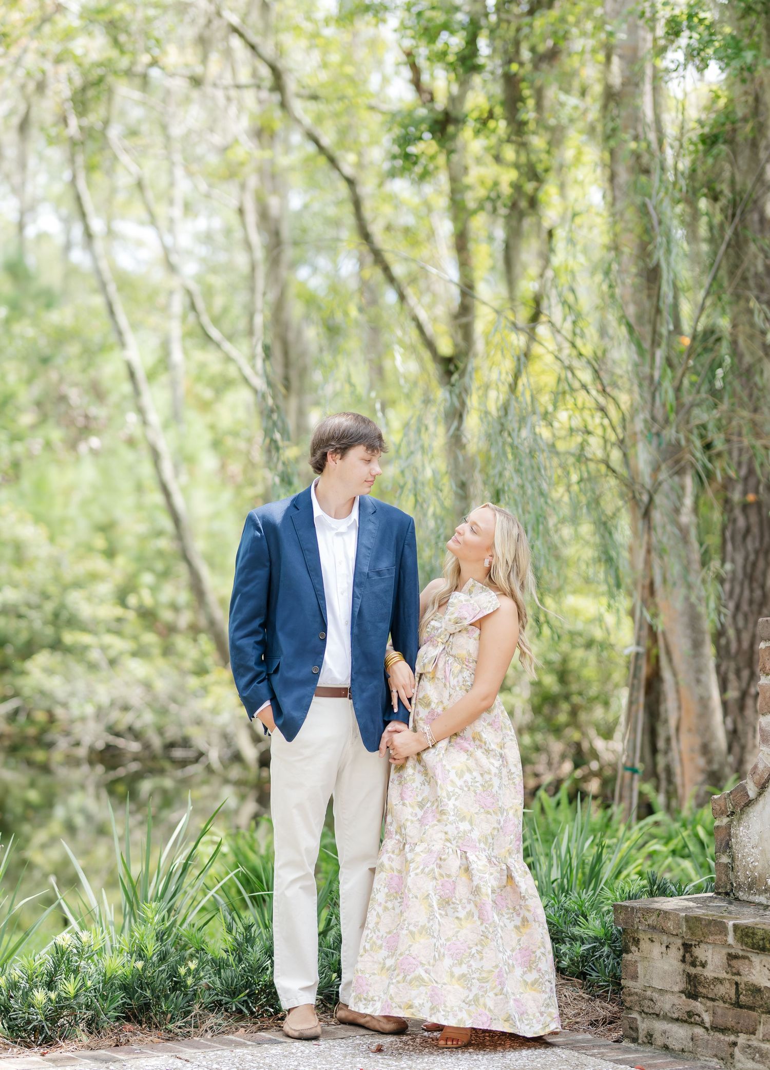 Romantic couple walking and posing together in a lush garden setting with Spanish moss hanging overhead.