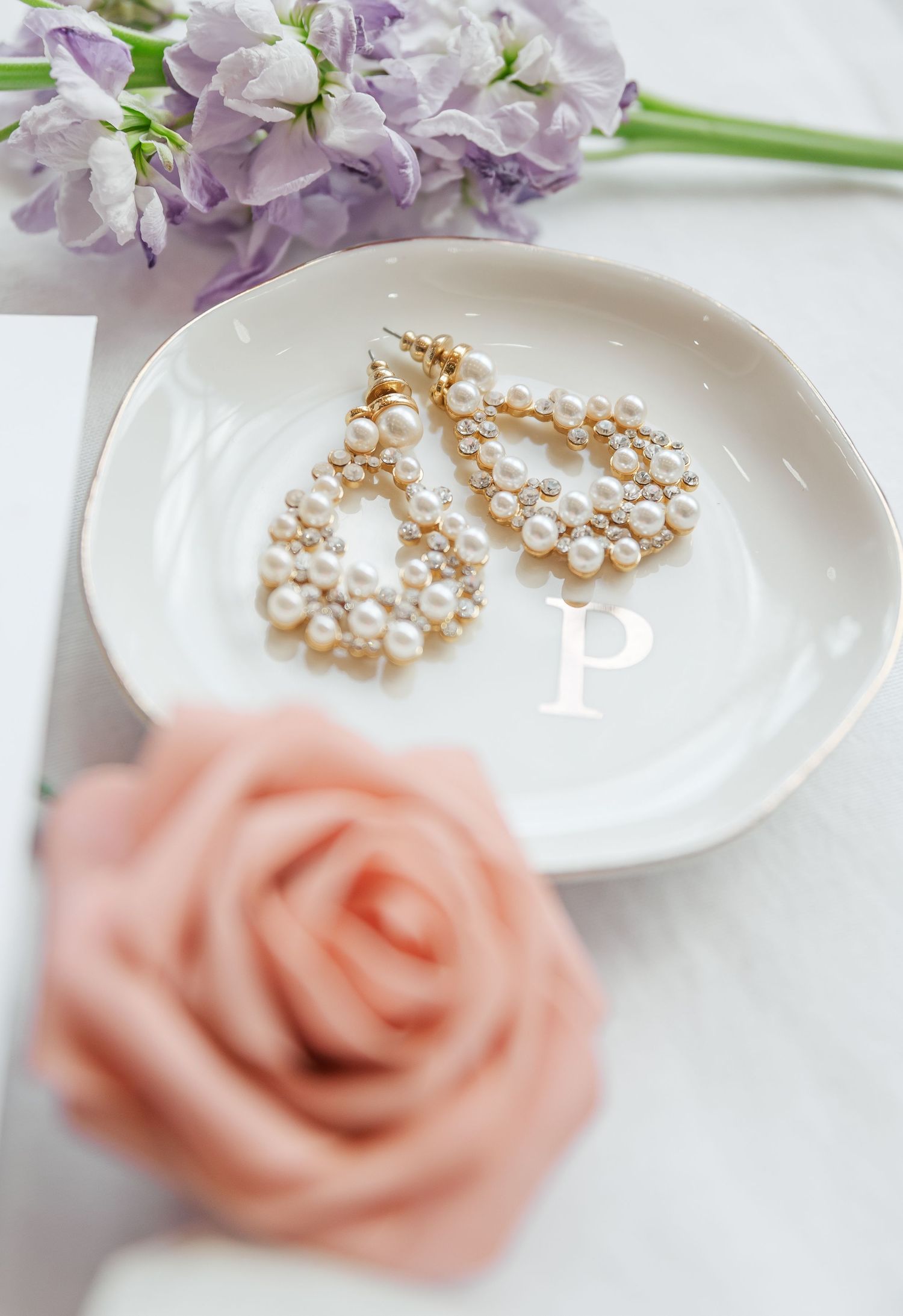 Pearl drop earrings on white plate with lavender flowers and coral rose accent.