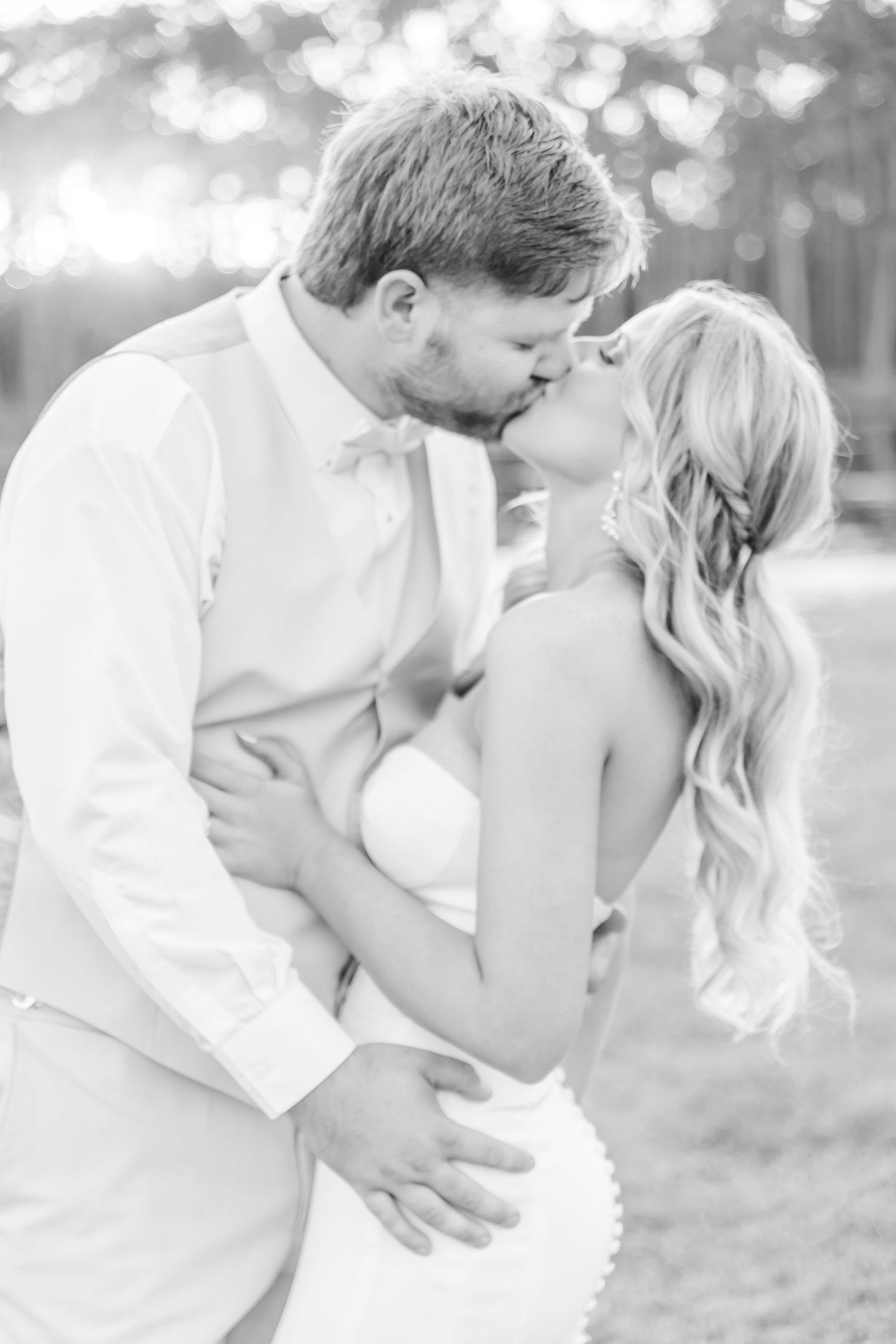 Black and white romantic portrait of newlyweds sharing a kiss in an outdoor setting.