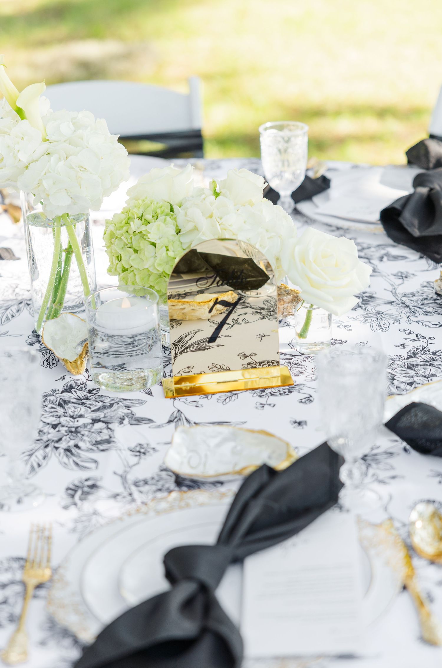 Elegant black and white toile tablecloth with gold accents, white floral centerpieces, and black ribbon napkins for a wedding reception.