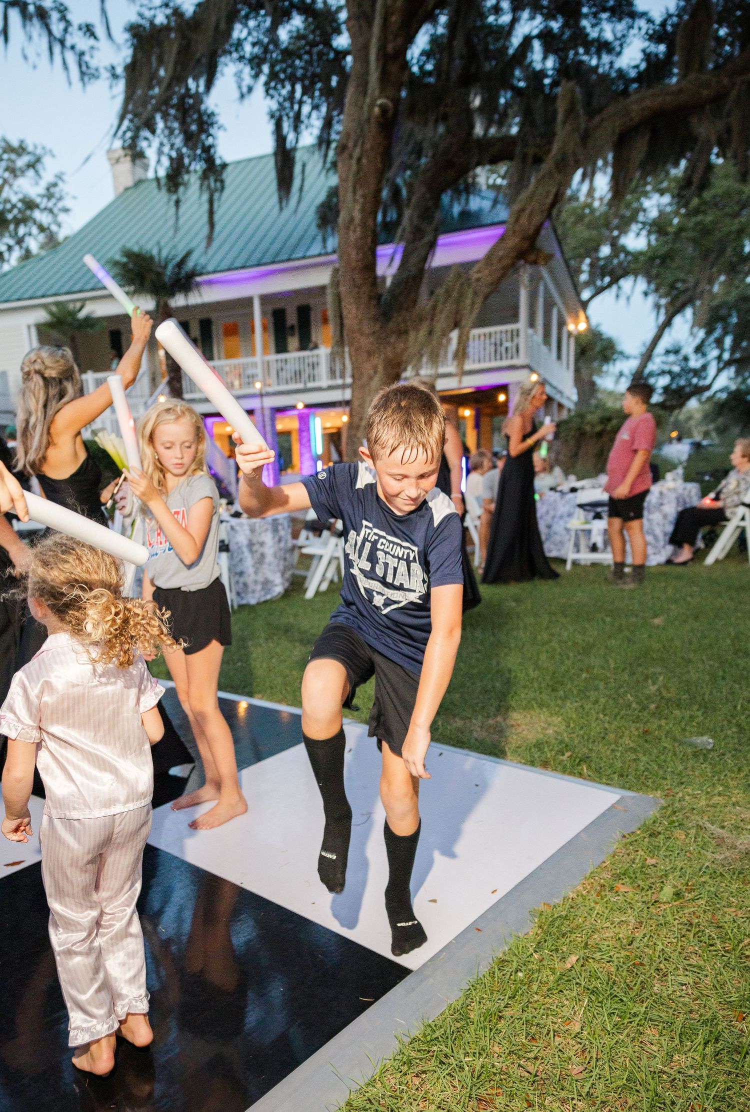 Children dancing and playing with glow sticks at an outdoor wedding reception on a dance floor.