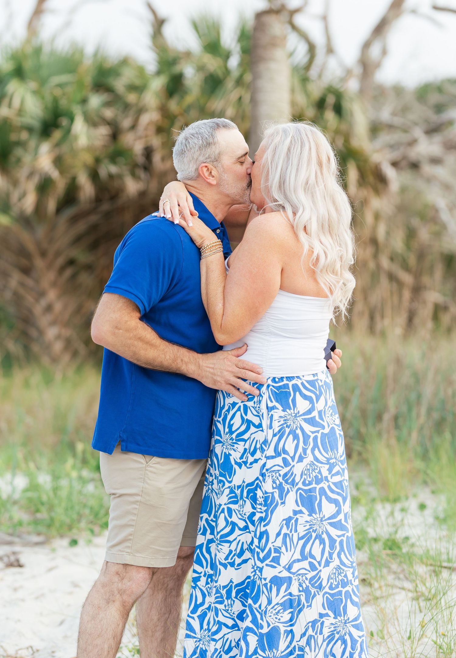 A tender kiss shared between a couple on a beach with palm trees in the background.