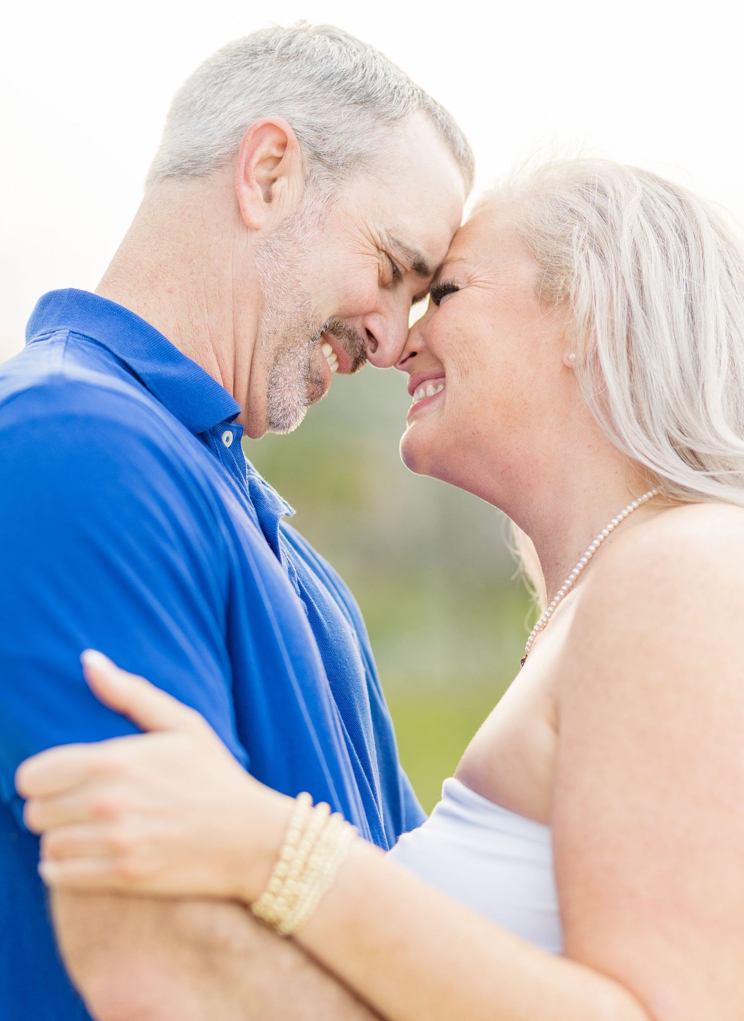 Loving mature couple in blue and white clothing sharing tender moments outdoors on a sunny day.