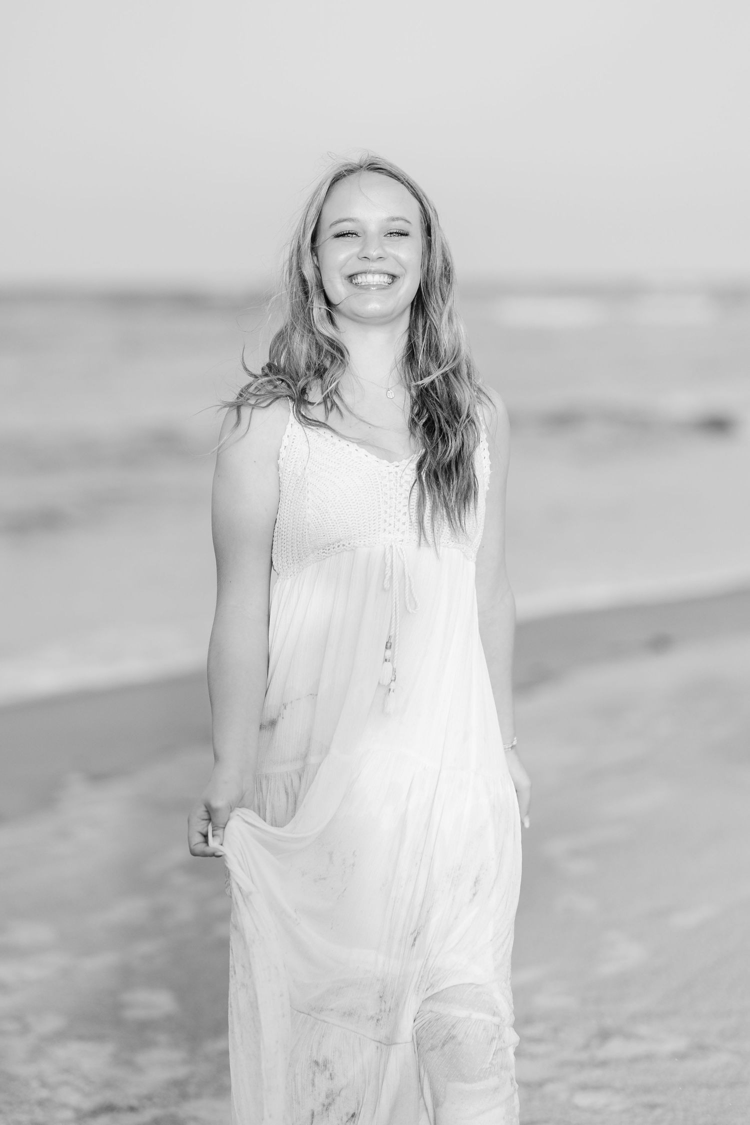 A flowing white dress creates an ethereal look in a black and white beach portrait session.