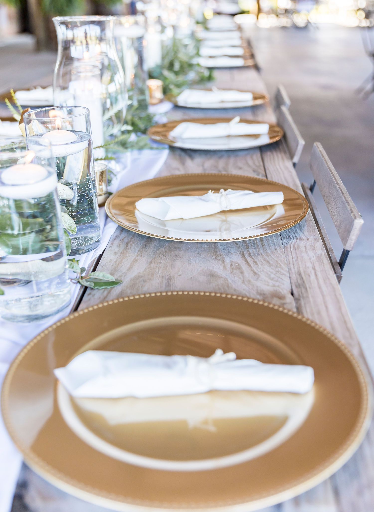 Close-up of gold charger plates with white napkins and greenery table runner.