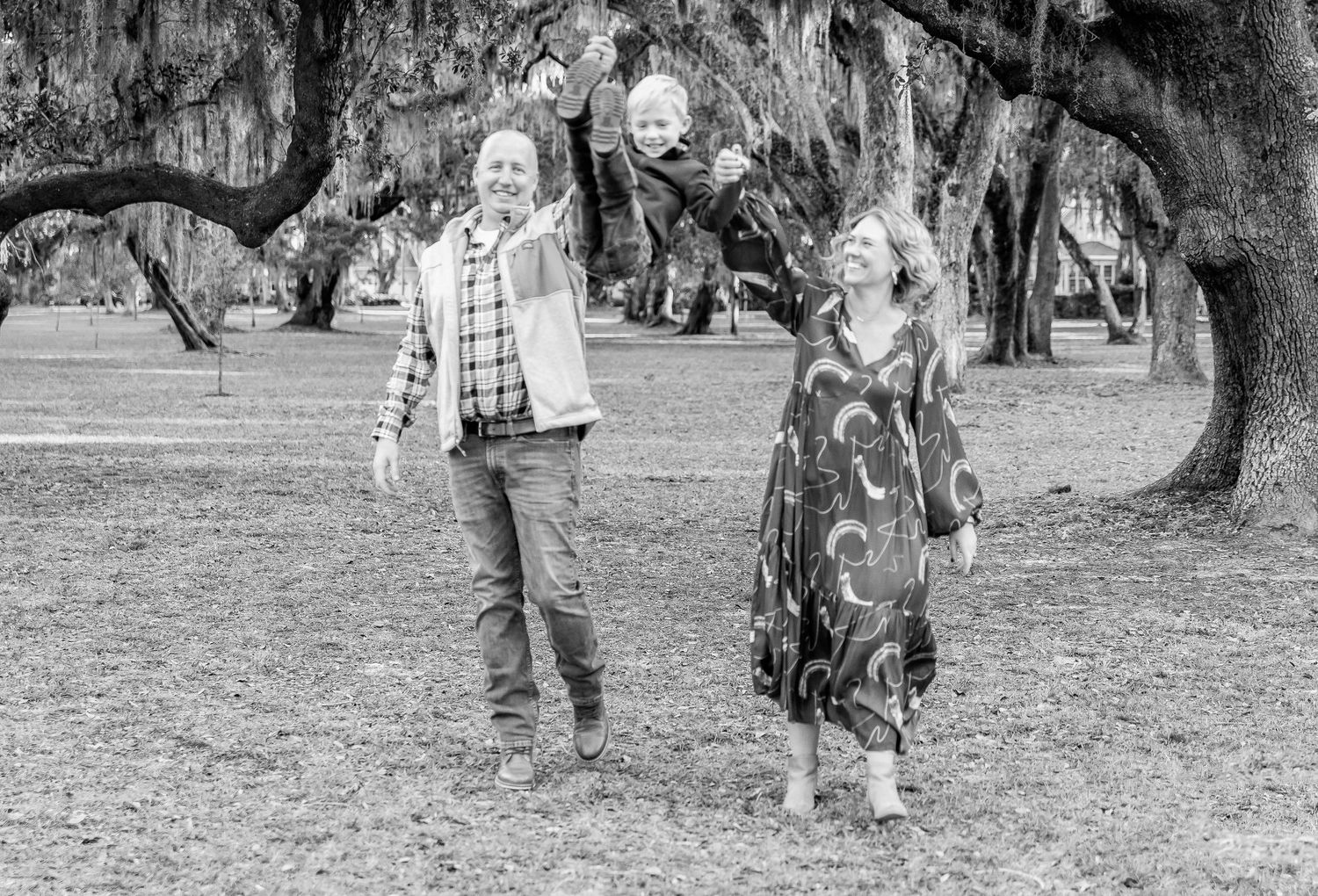 Black and white photo of couple enjoying playful moment under oak trees.