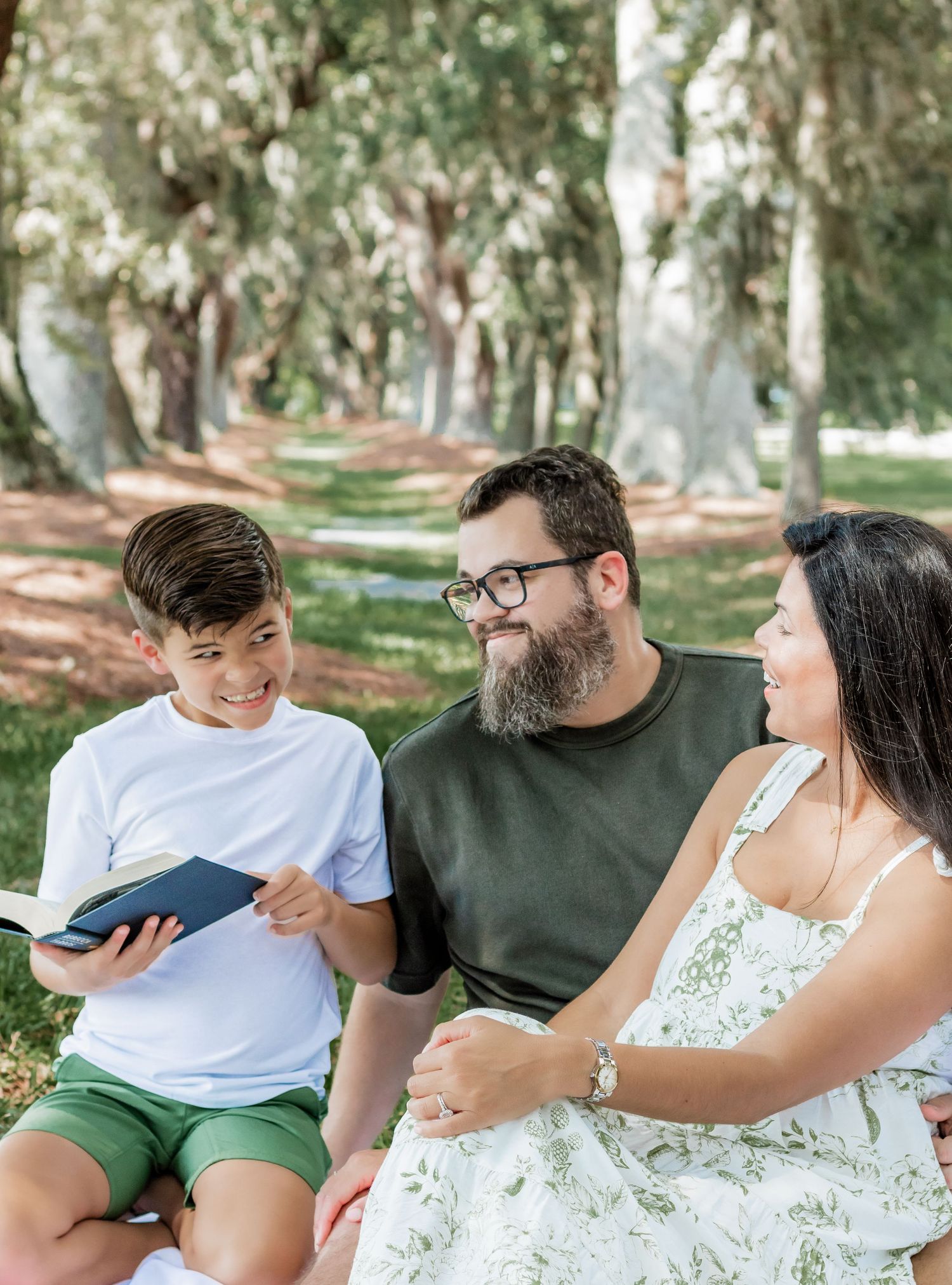 Family reading together during a picnic in a wooded park setting.