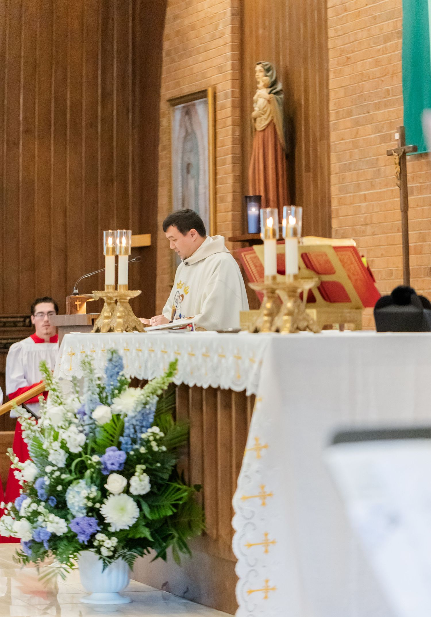 Catholic wedding ceremony altar with priest, flowers and golden candlesticks.